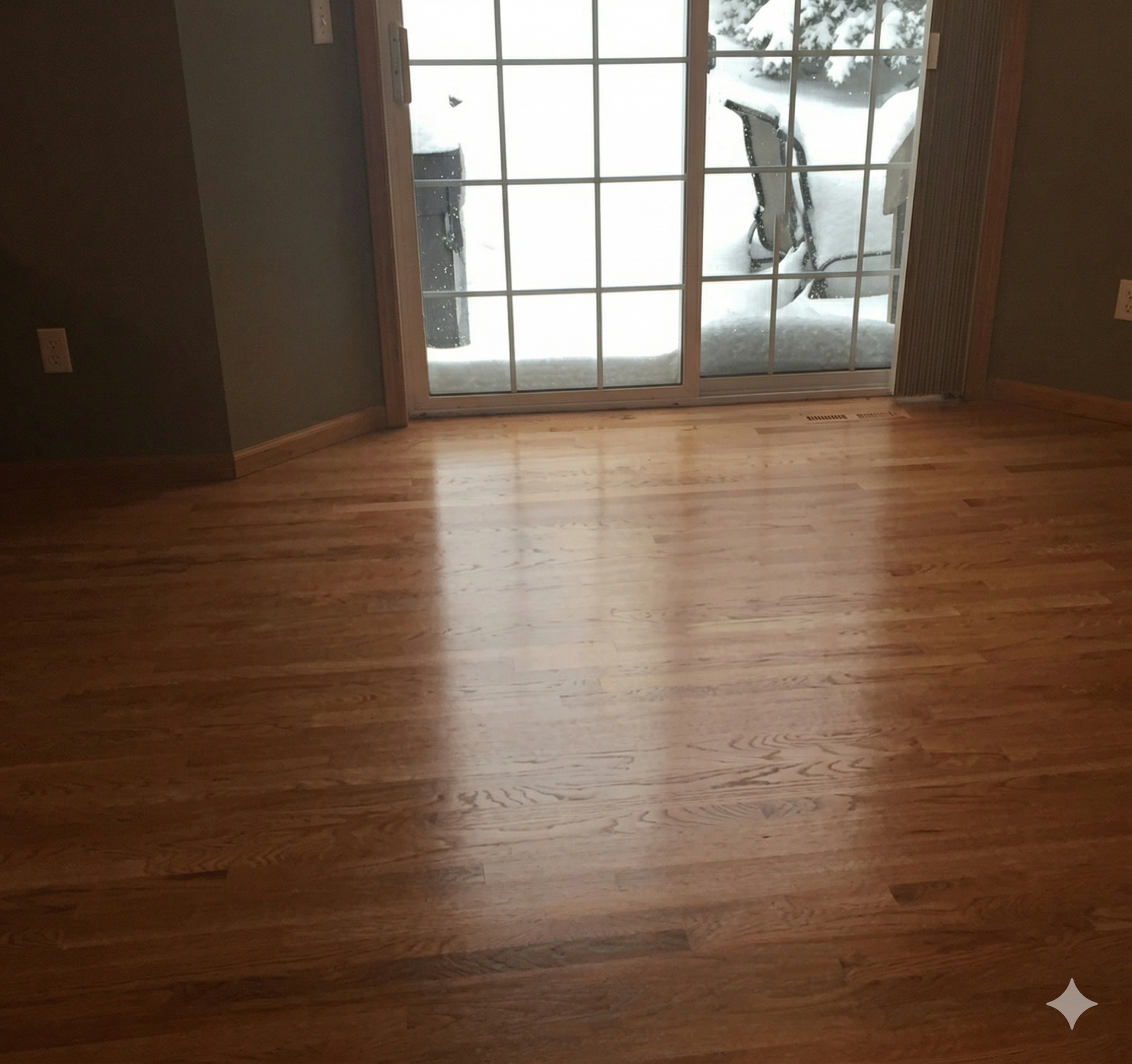 A polished hardwood floor in a room, with a glass sliding door looking out onto a snow-covered patio.