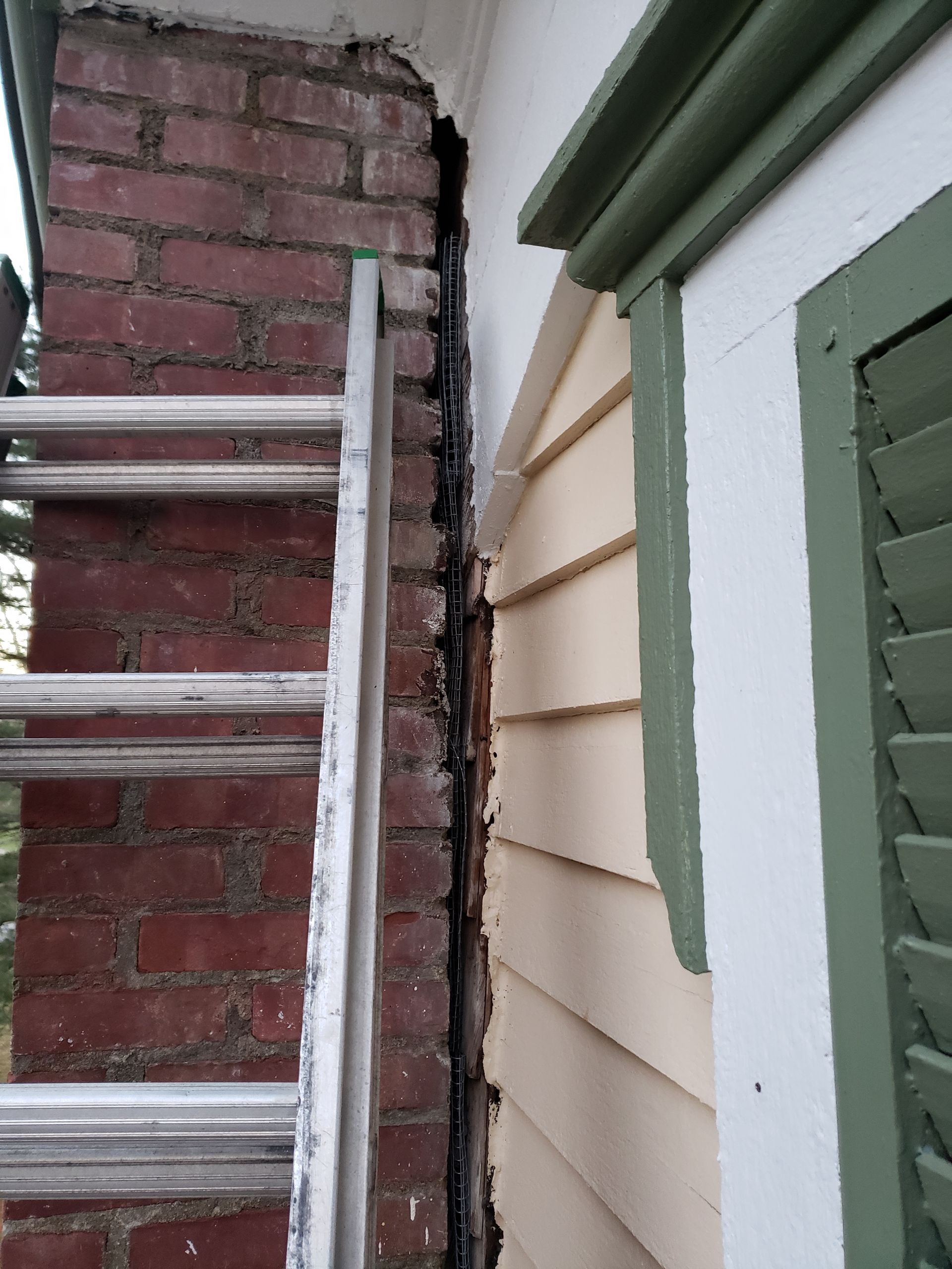 A ladder is leaning against a brick wall next to a window.