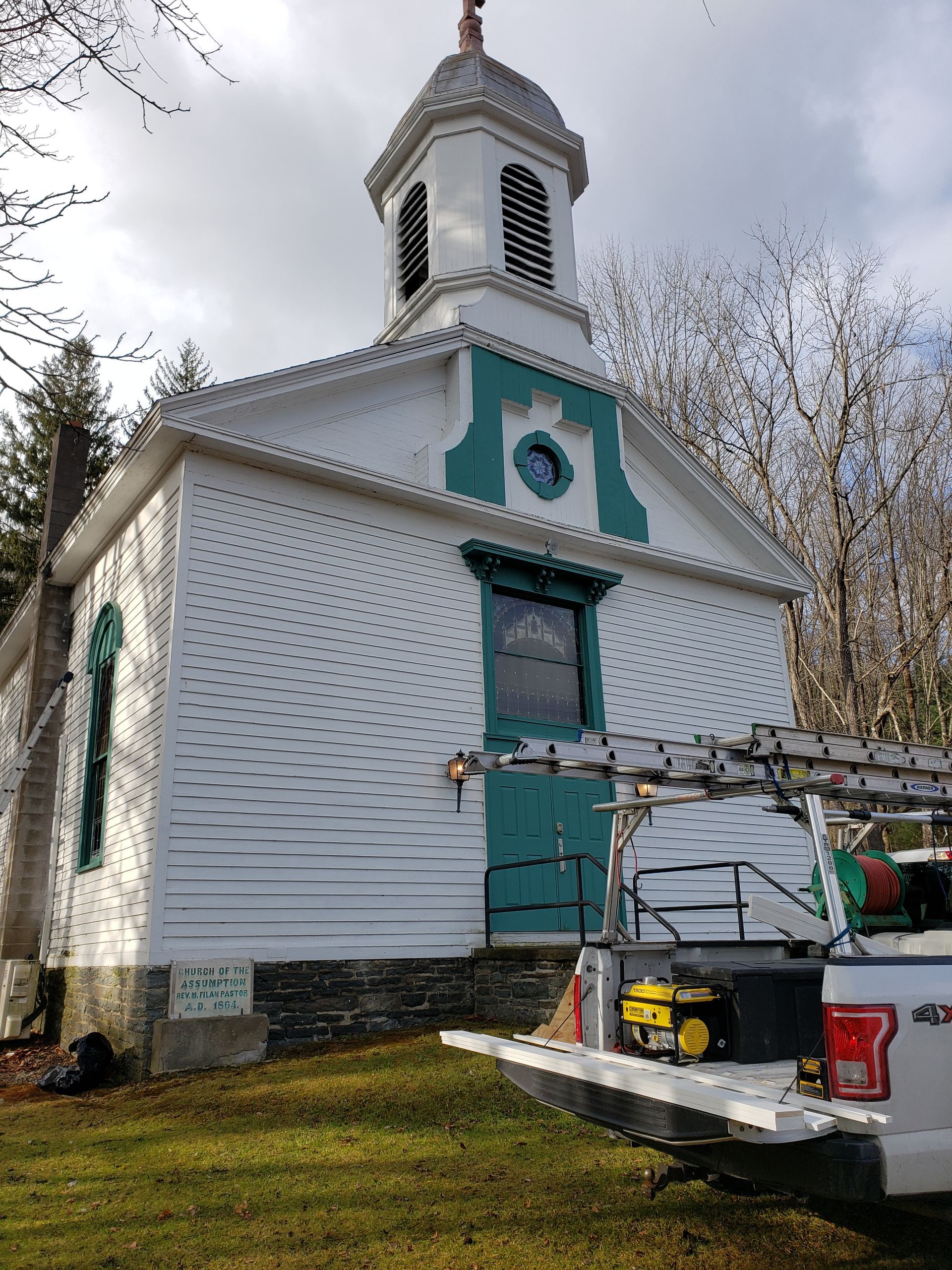 A white truck is parked in front of a white and green church.