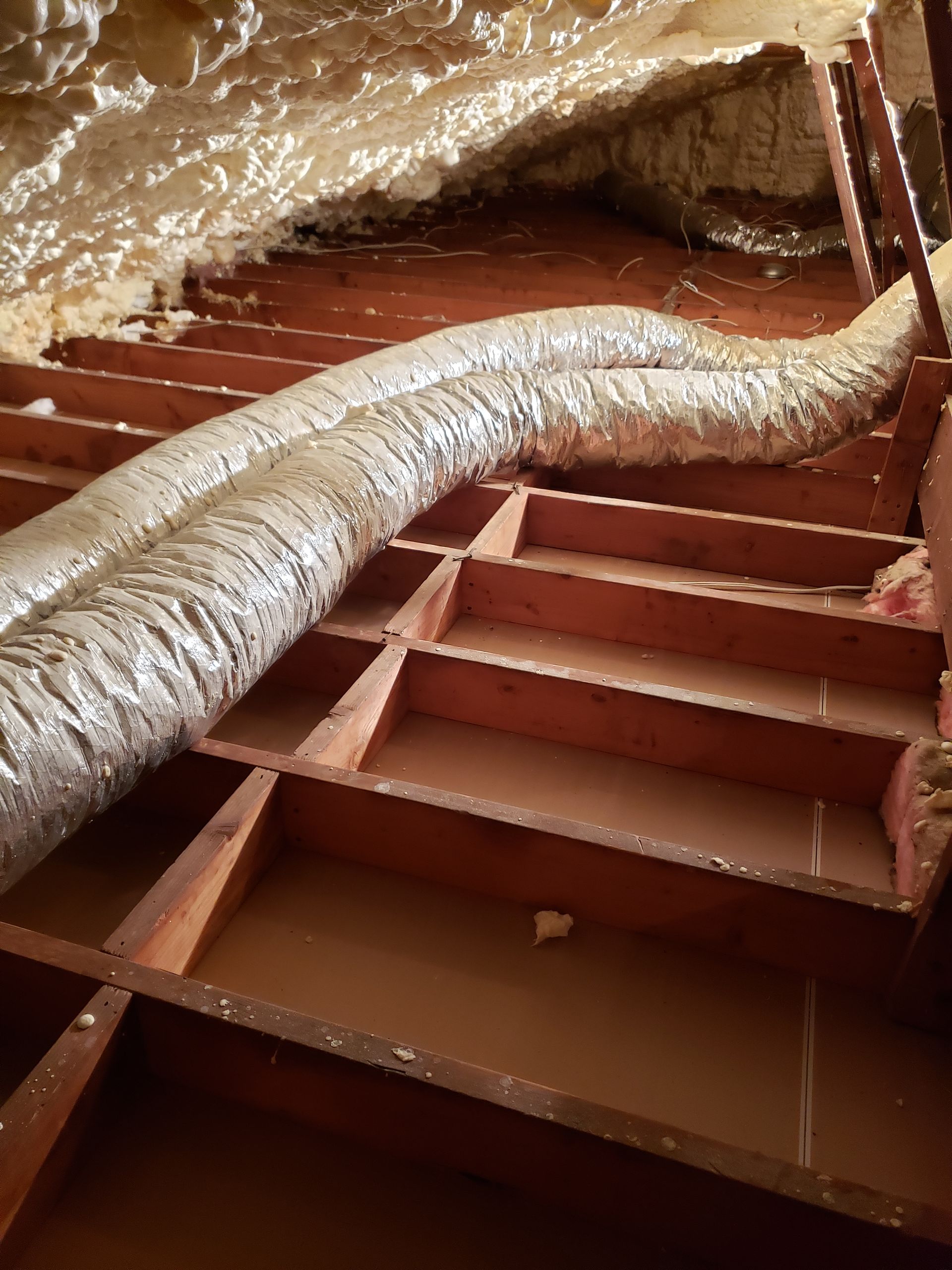 A duct is hanging from the ceiling of an attic.