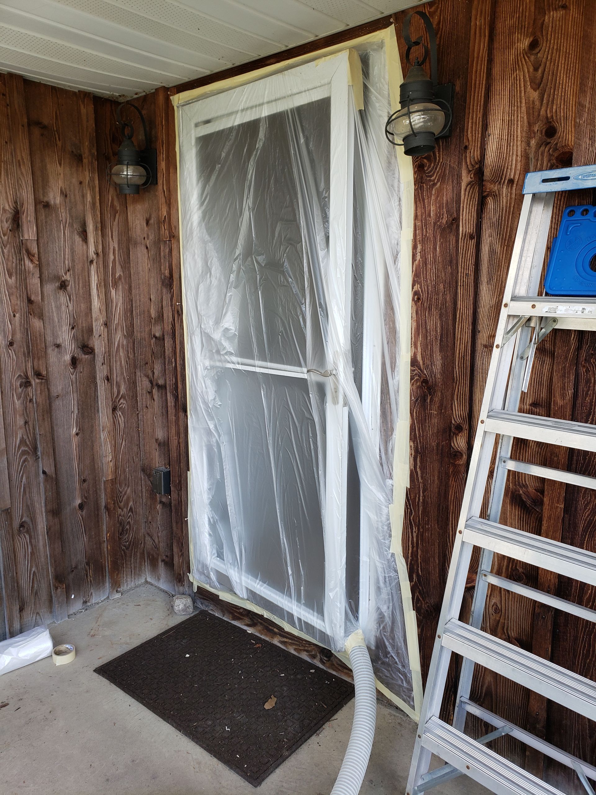 A door is covered in plastic and a ladder is next to it.