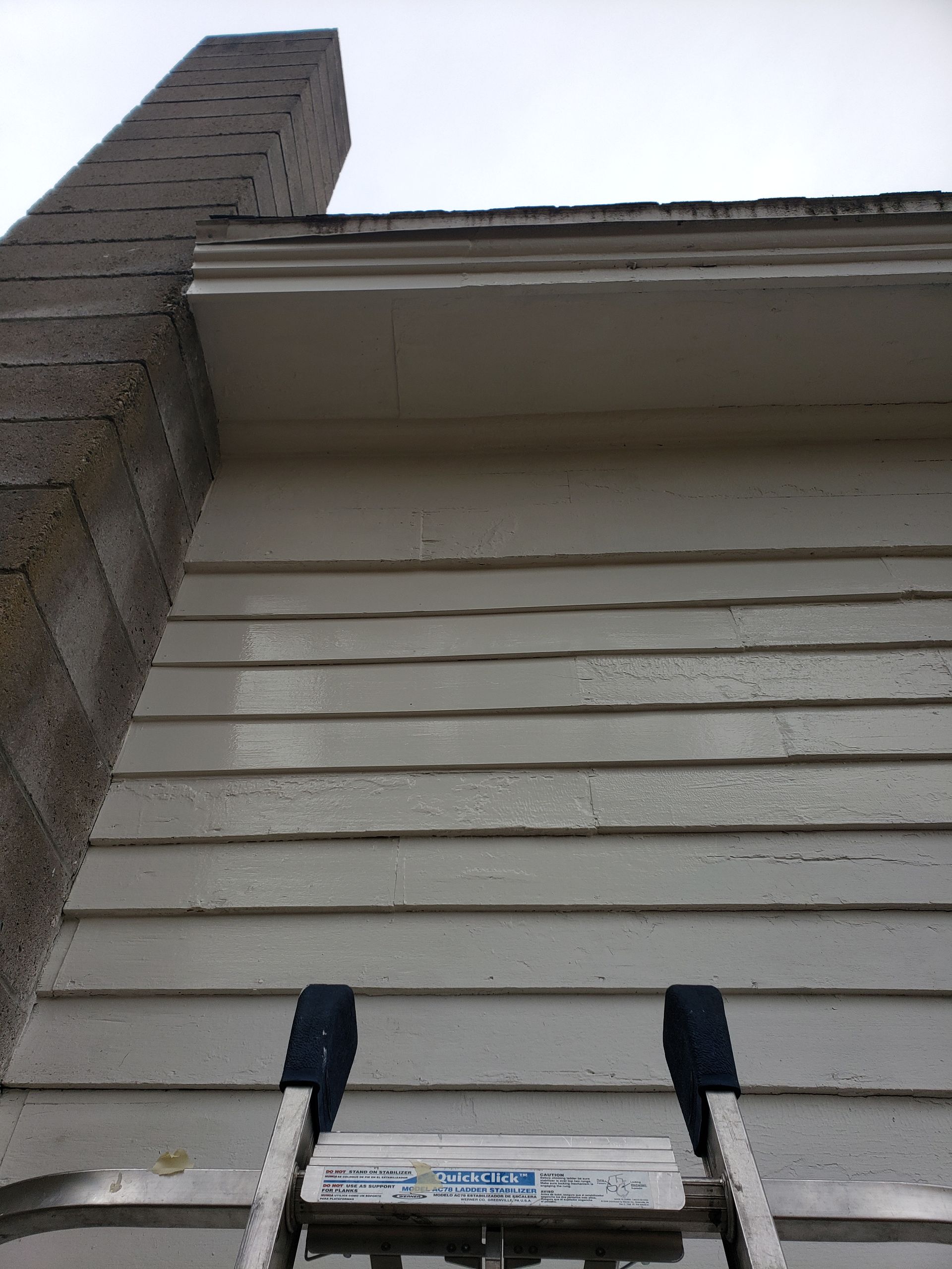 A ladder is sitting on the side of a house next to a chimney.
