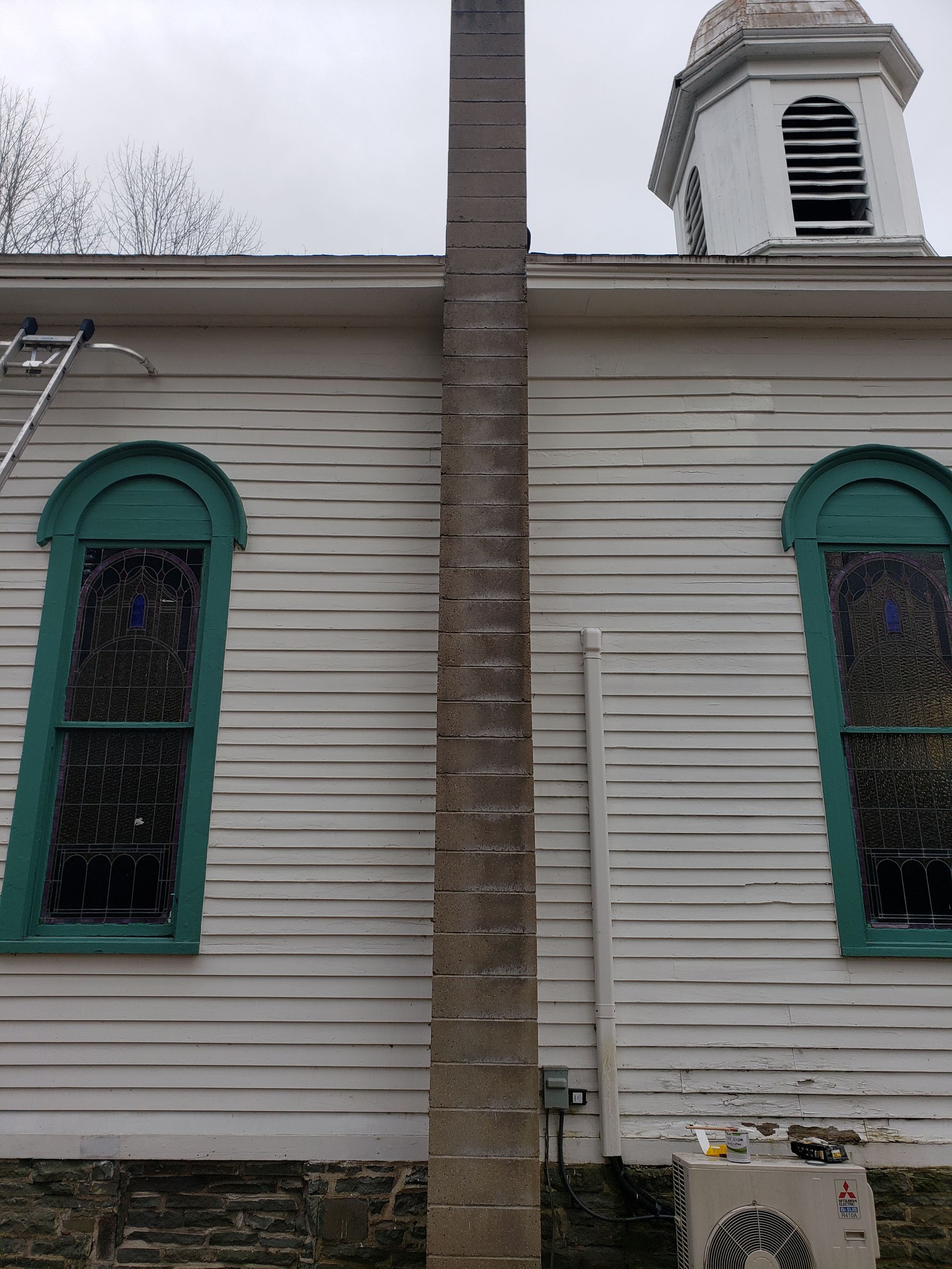 A white building with green windows and a chimney on the side.