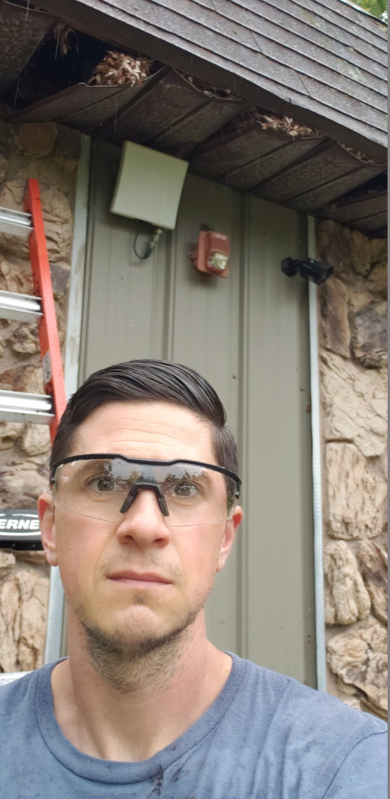 A man wearing safety glasses is taking a selfie in front of a building.