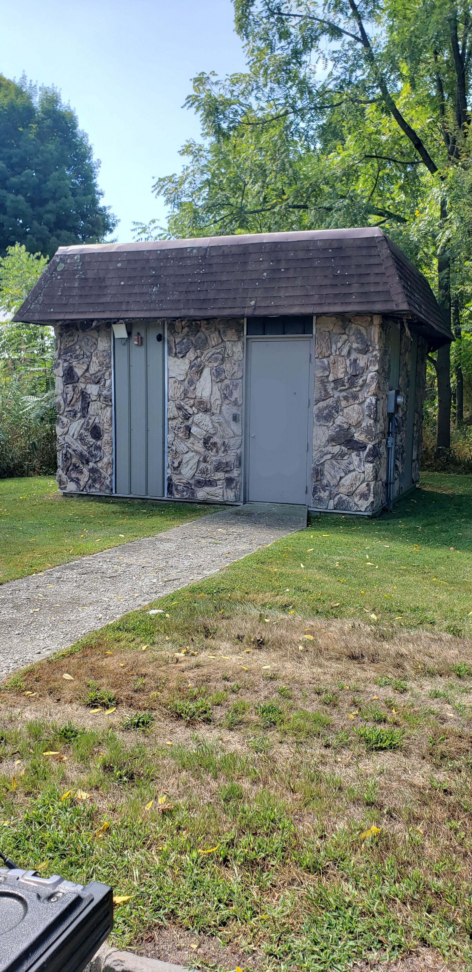 A small stone building with a roof is sitting in the middle of a grassy field.