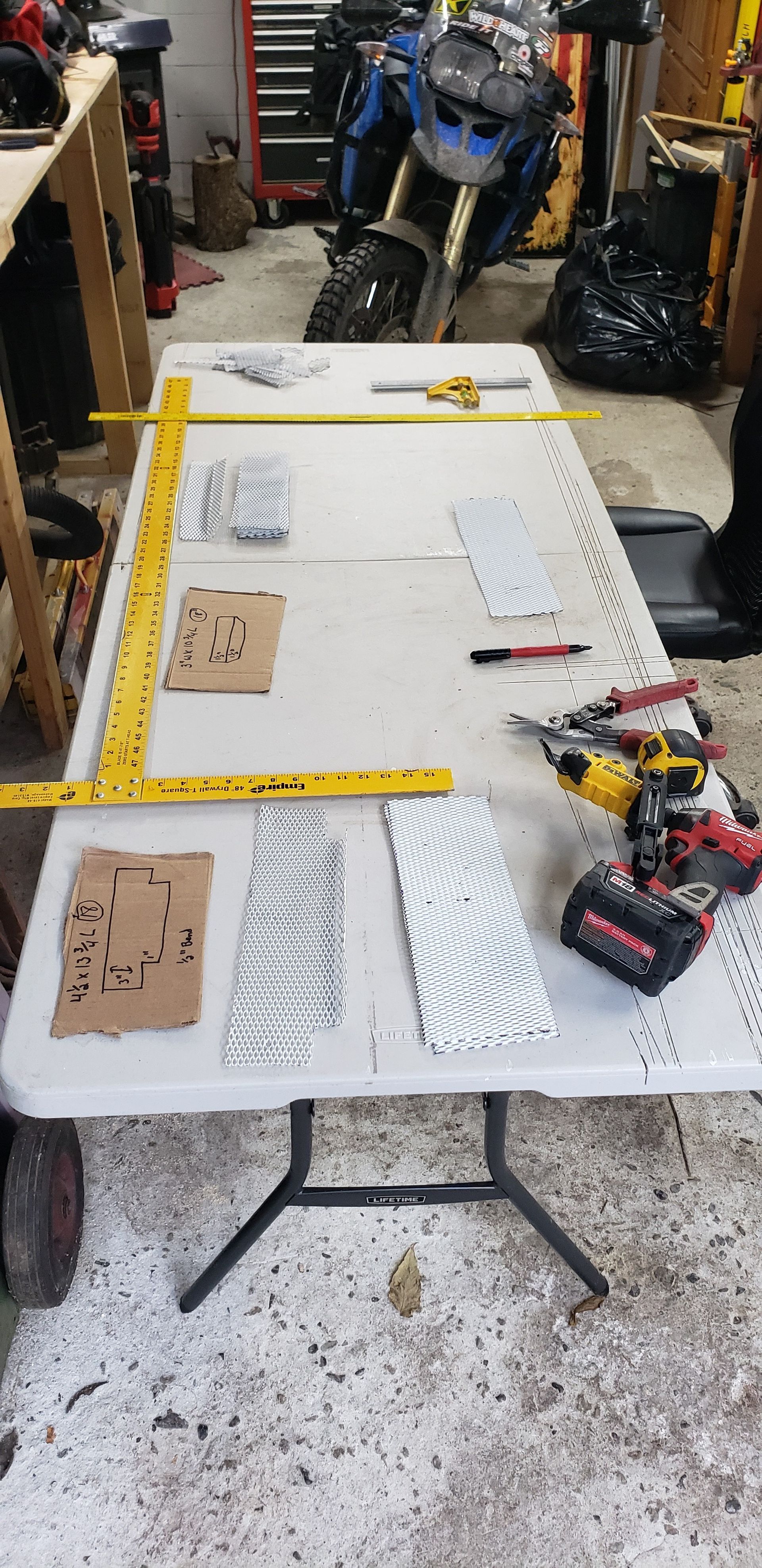 A folding table with a ruler and a drill on it in a garage with a motorcycle in the background.