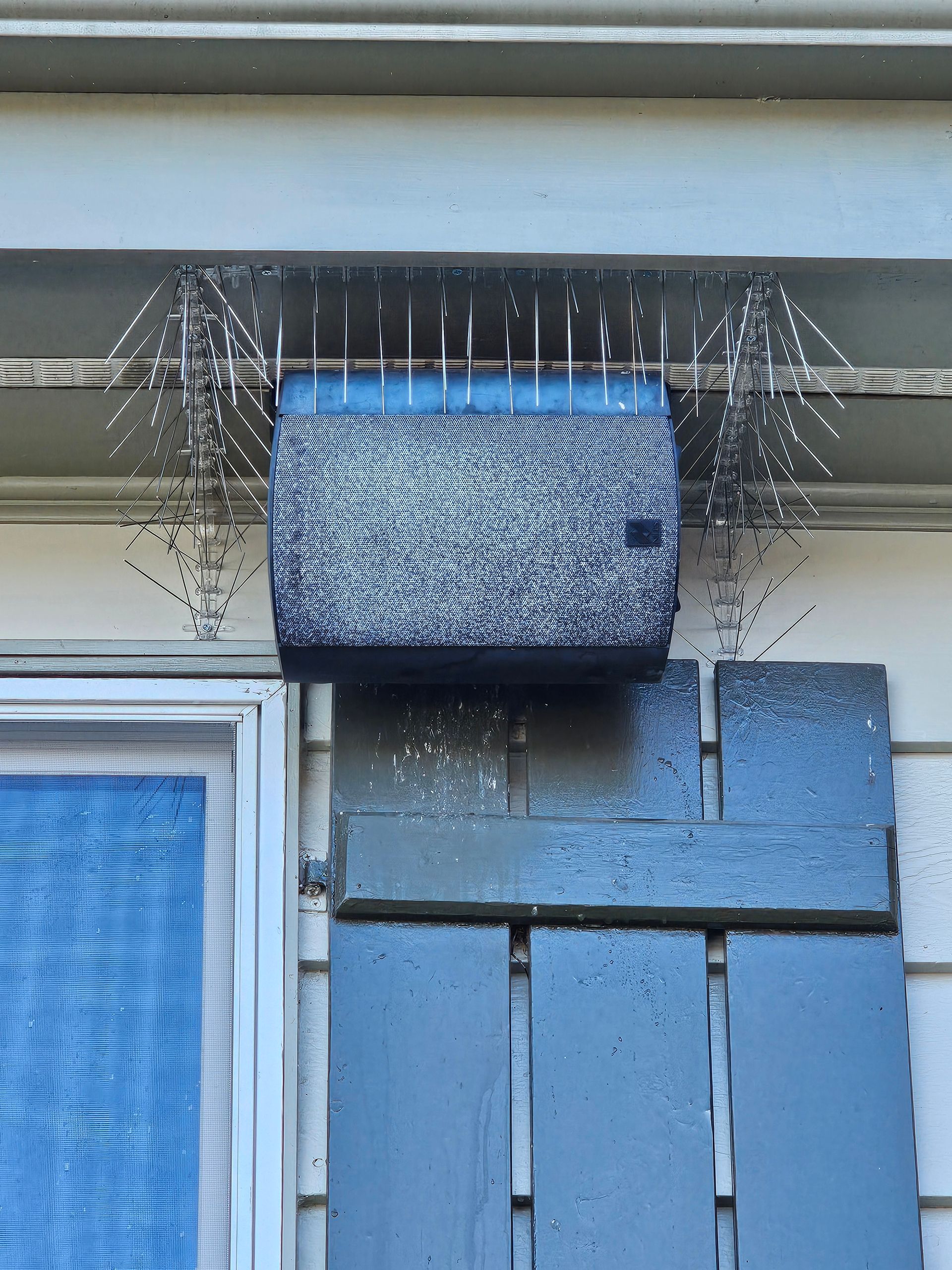 A blue container is hanging from the roof of a house