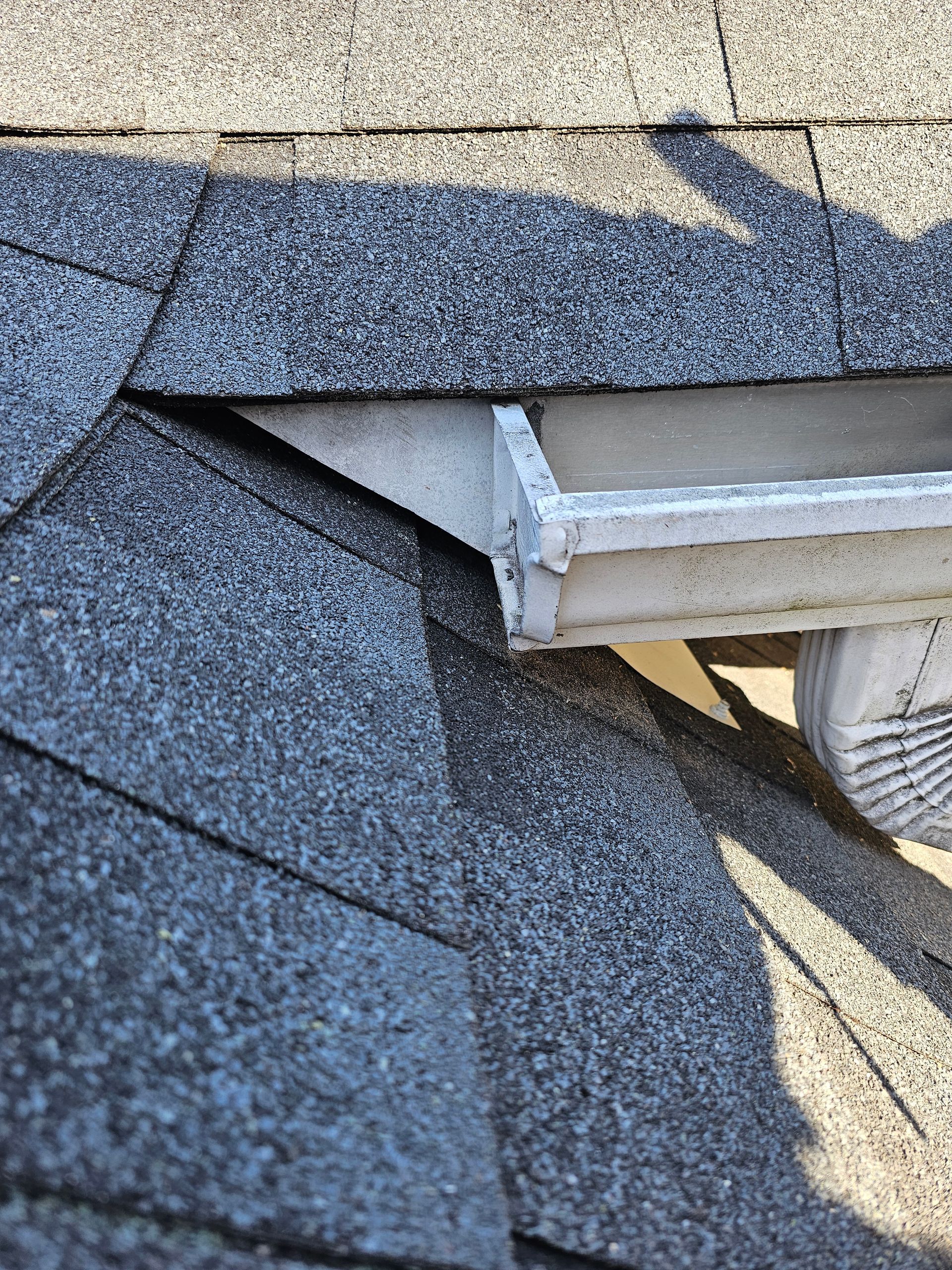 A close up of a gutter on a roof with shingles.