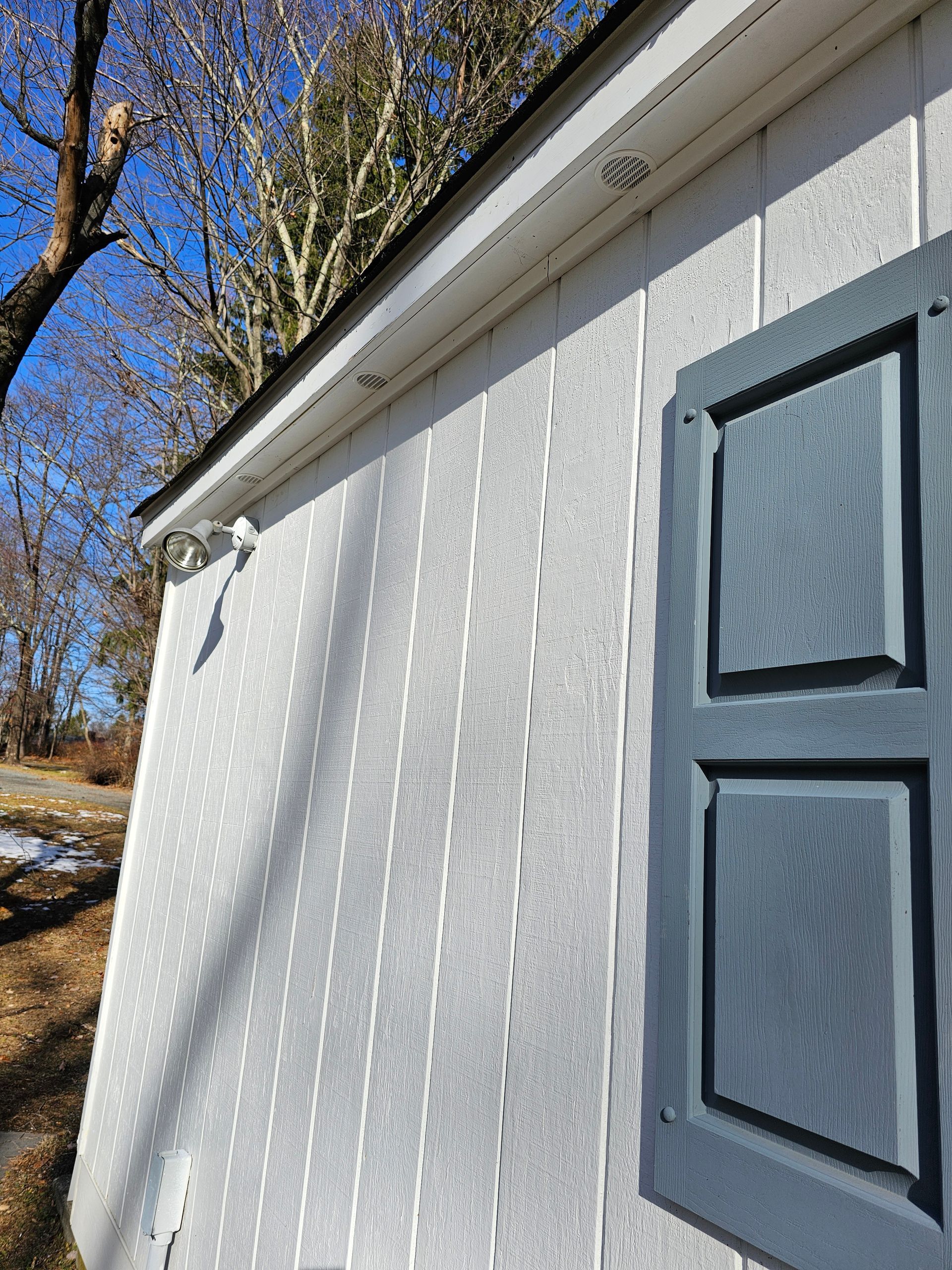 A white shed with a window and shutters on it.