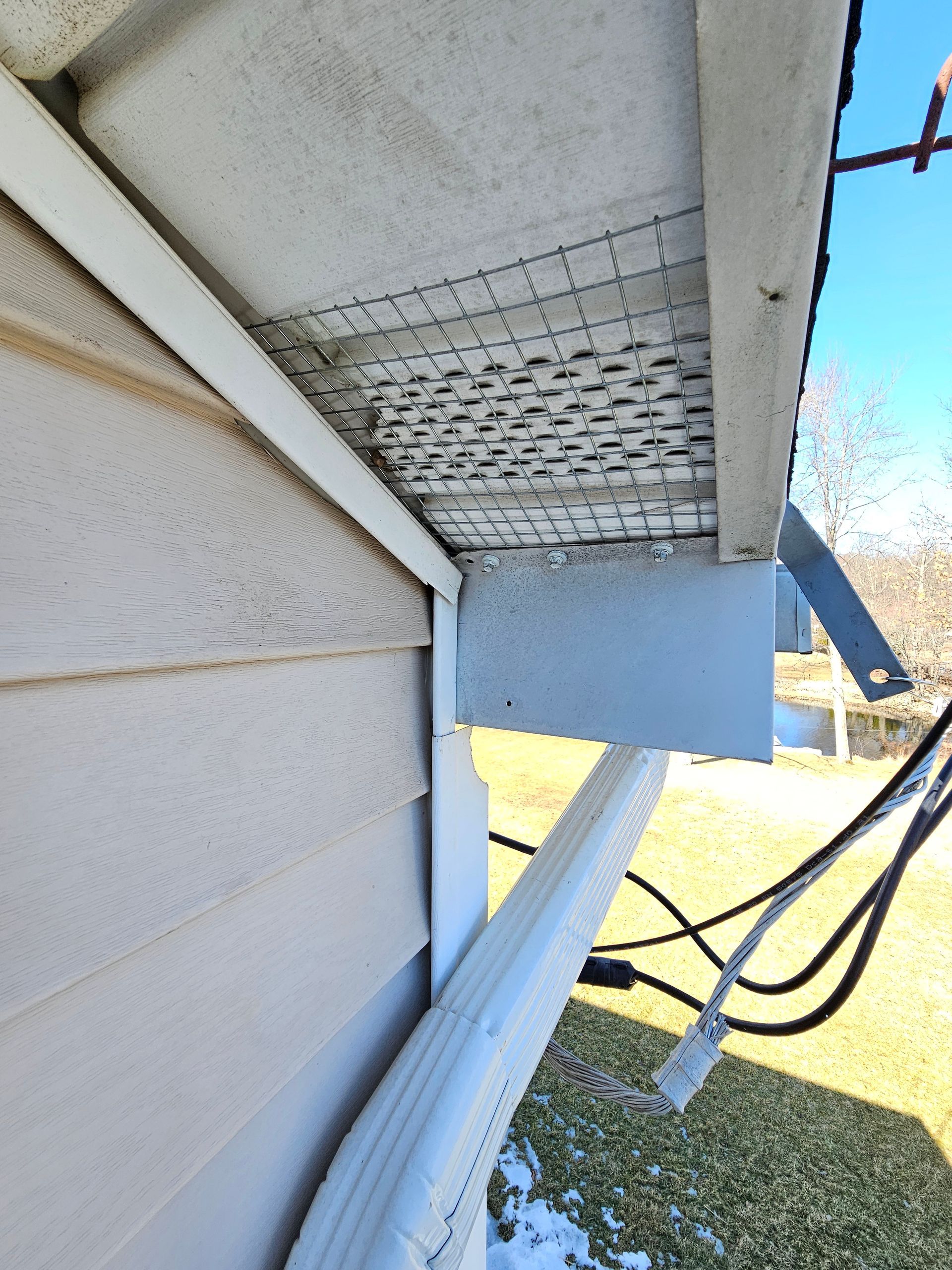 A gutter on the side of a house with a lot of wires coming out of it.