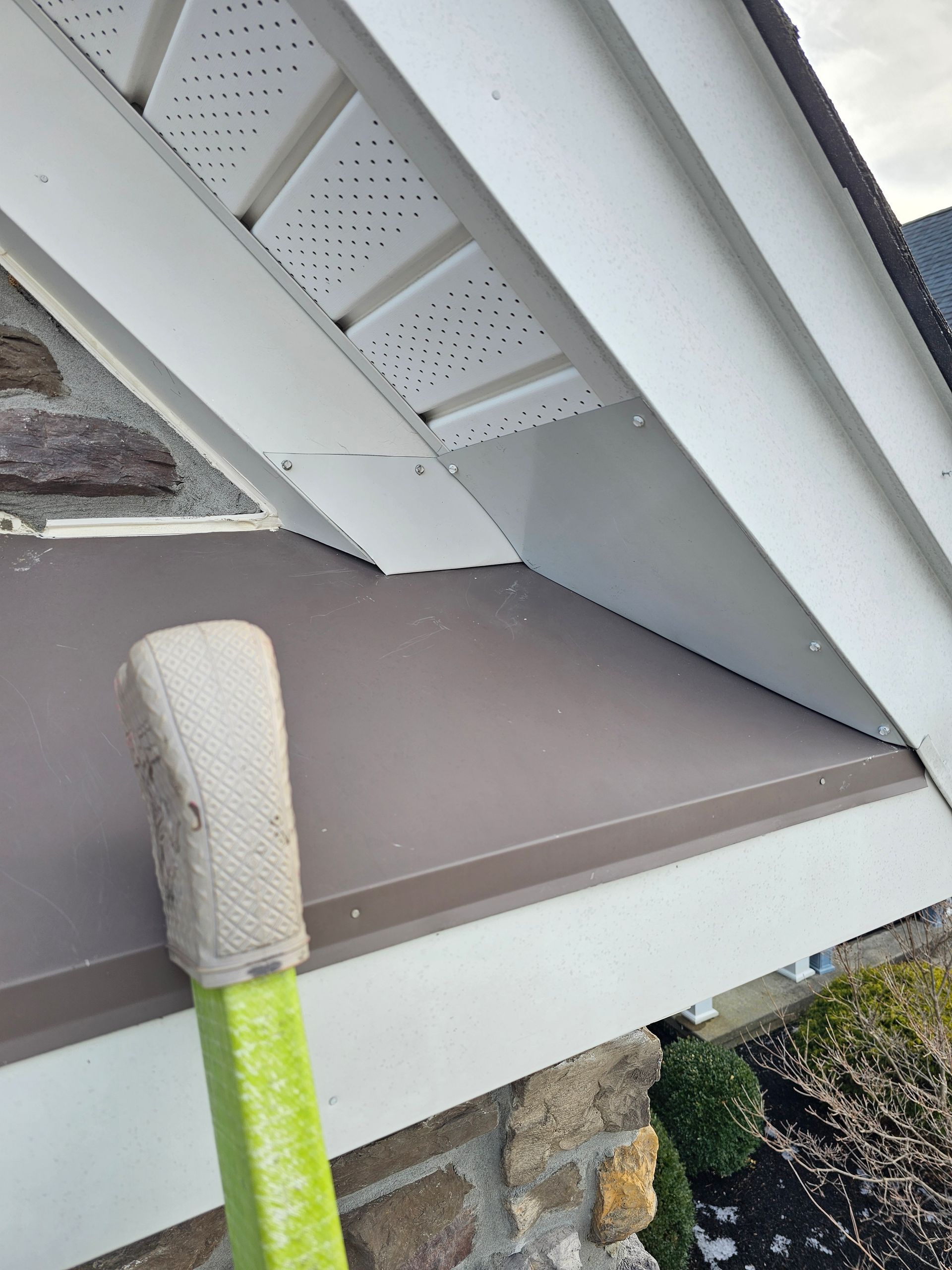 A green ladder is leaning against the roof of a house.