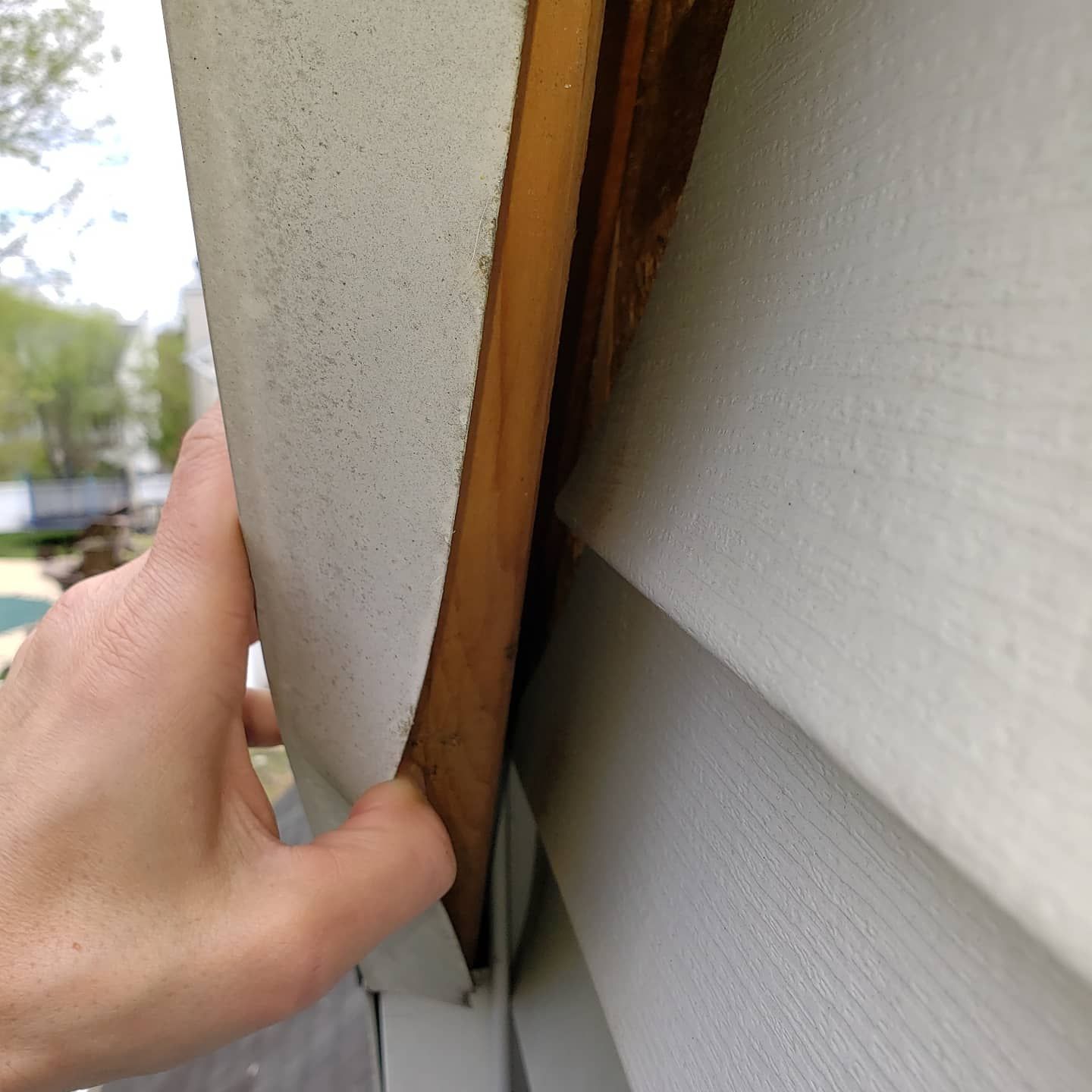 A person is holding a piece of wood on the side of a house.