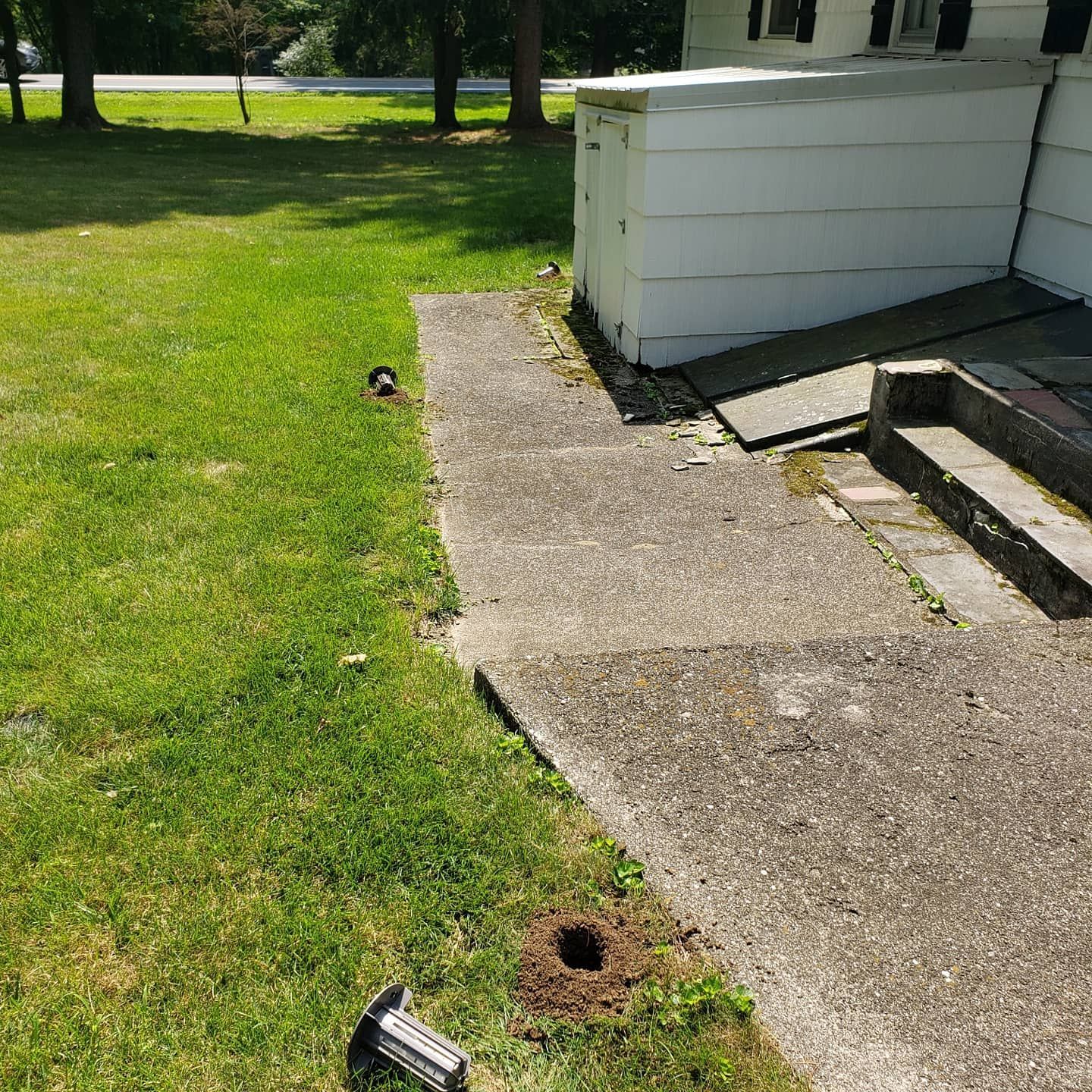 There is a hole in the grass next to a sidewalk.