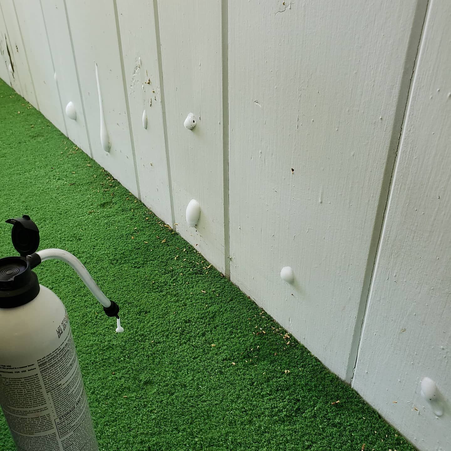 A spray bottle is sitting on the grass next to a white fence.