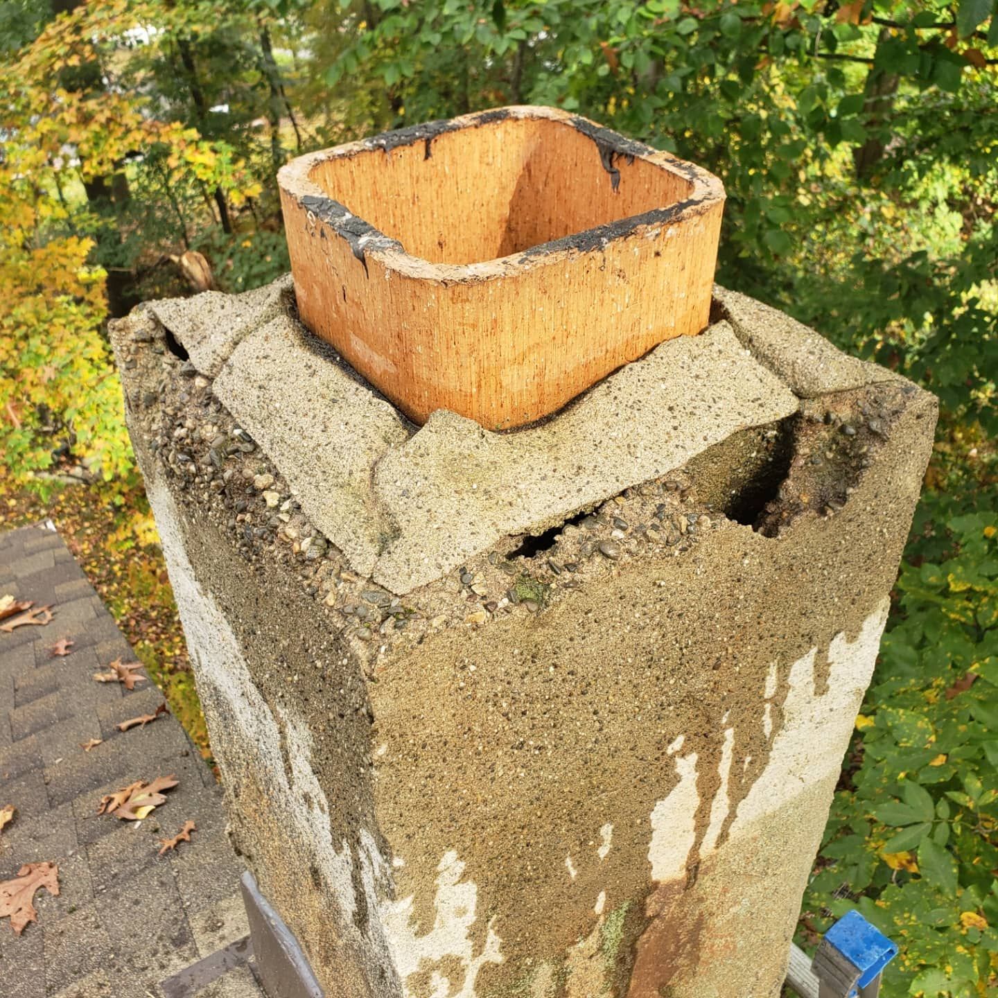 A chimney is sitting on top of a roof with trees in the background.