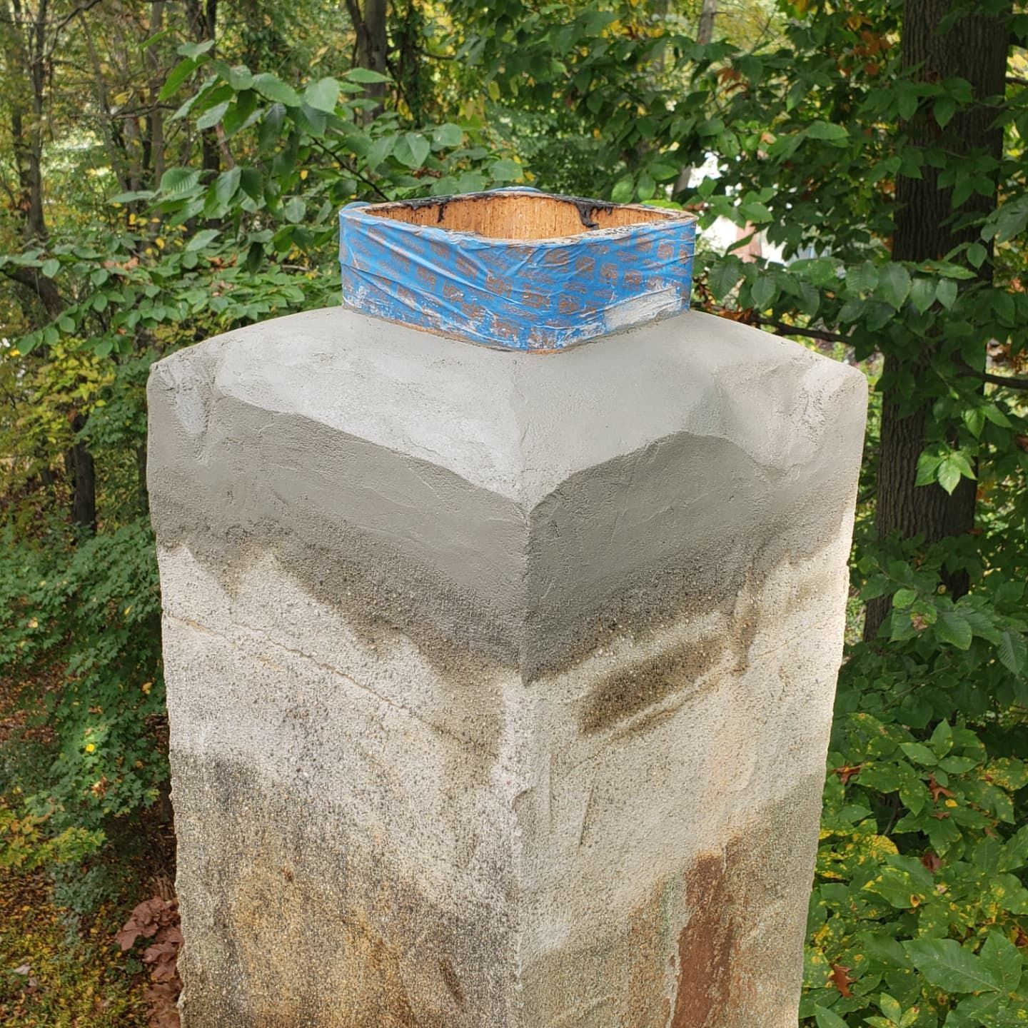 A stone chimney with a blue tape covering the top of it.