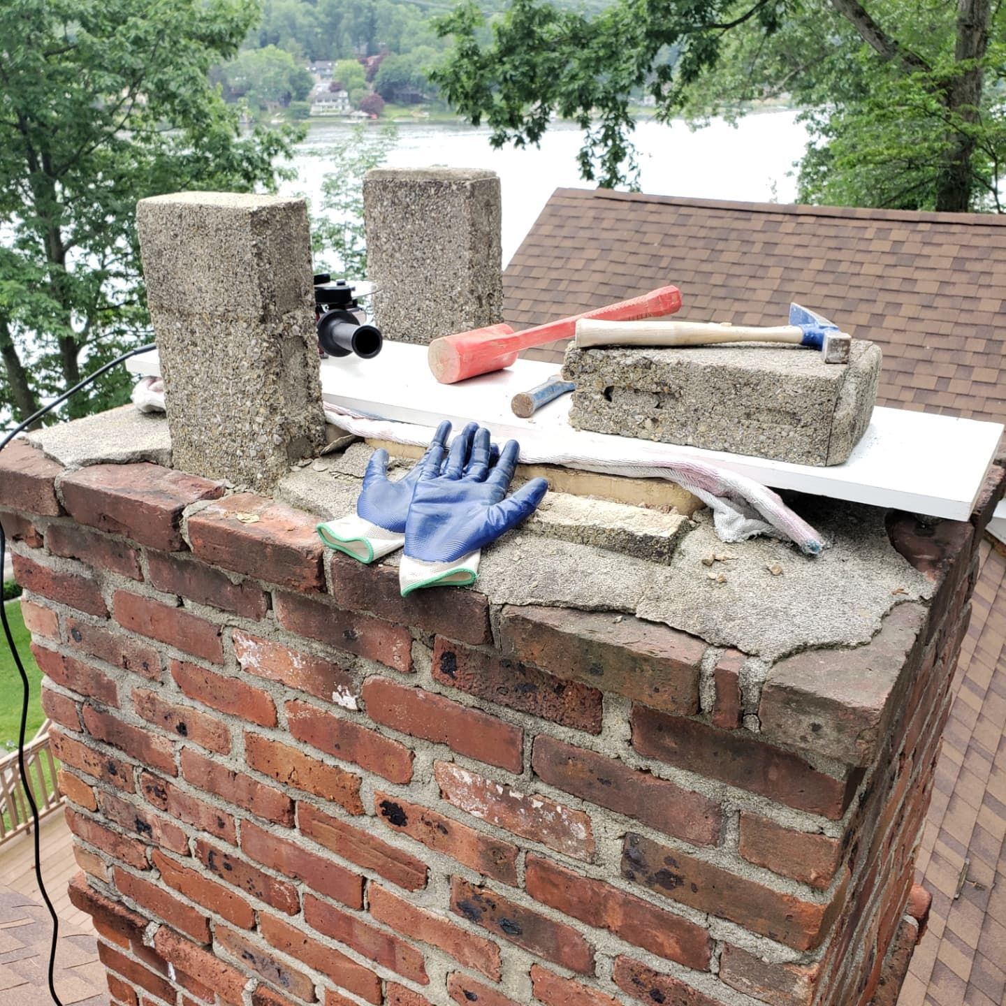 A brick chimney with a hammer and gloves on top of it.
