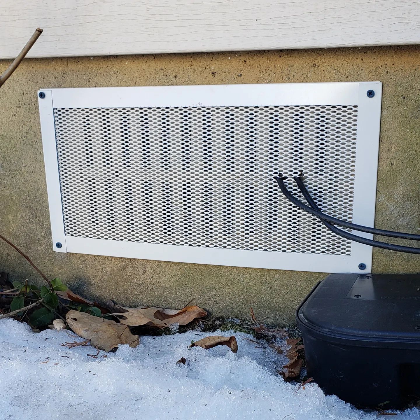 A metal grille on the side of a building with wires coming out of it.