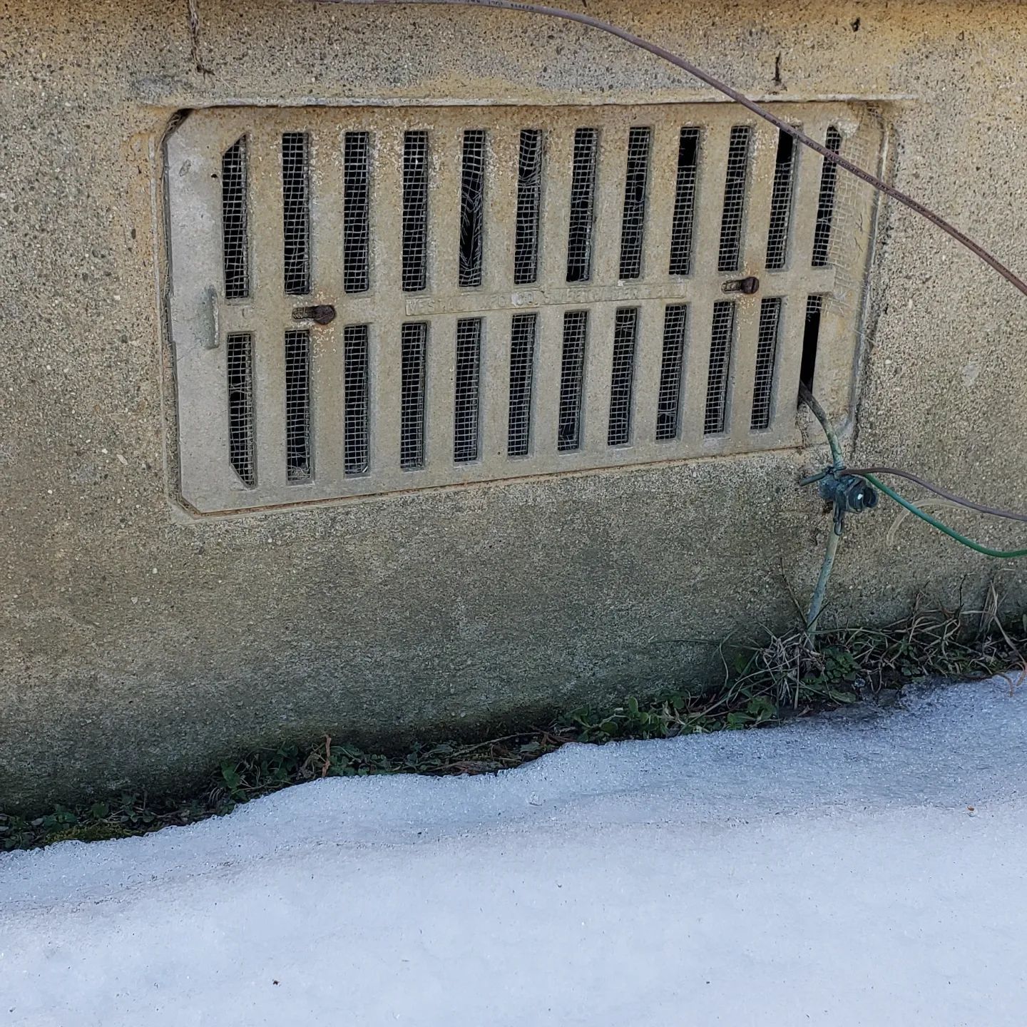 A drain on the side of a building with snow on the ground
