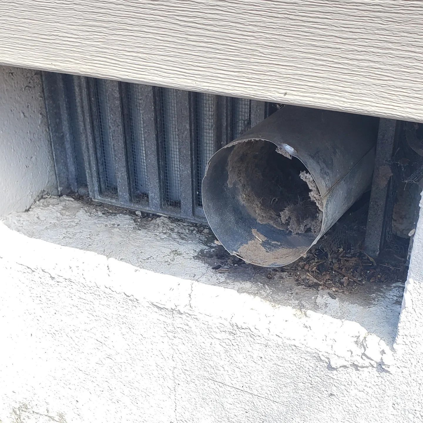 A dirty pipe is sitting under a concrete wall.