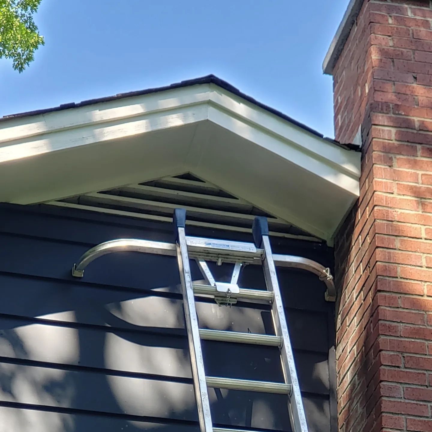 A ladder is attached to the side of a house next to a chimney.