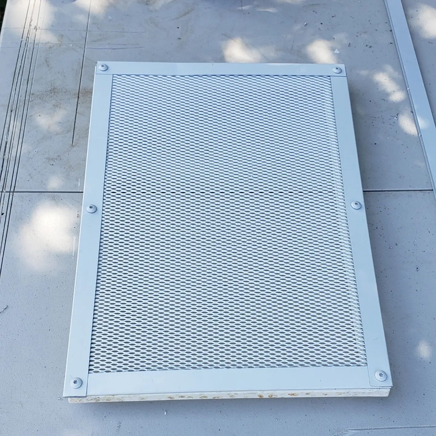 A white metal mesh is sitting on a concrete surface