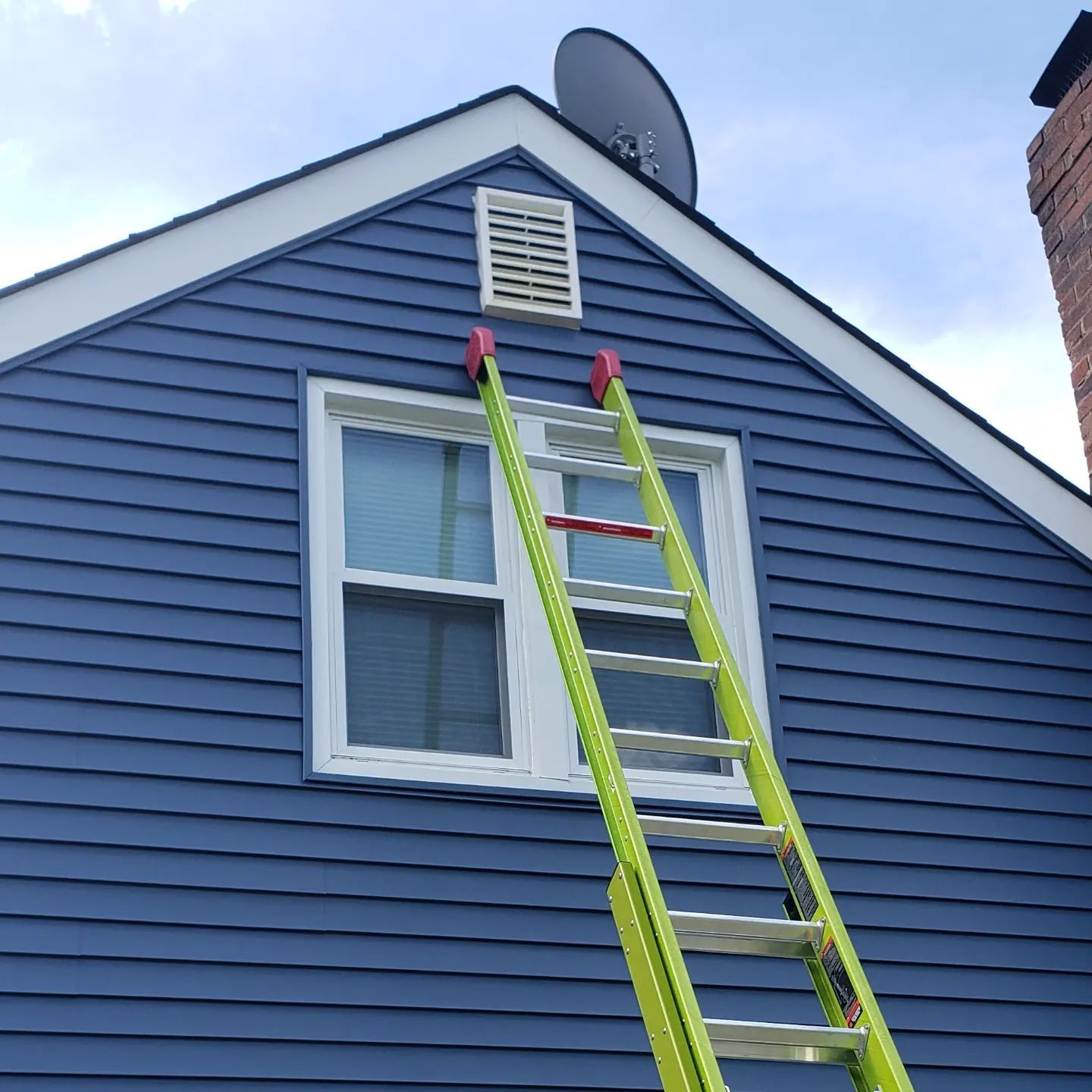 A green ladder is attached to the side of a blue house