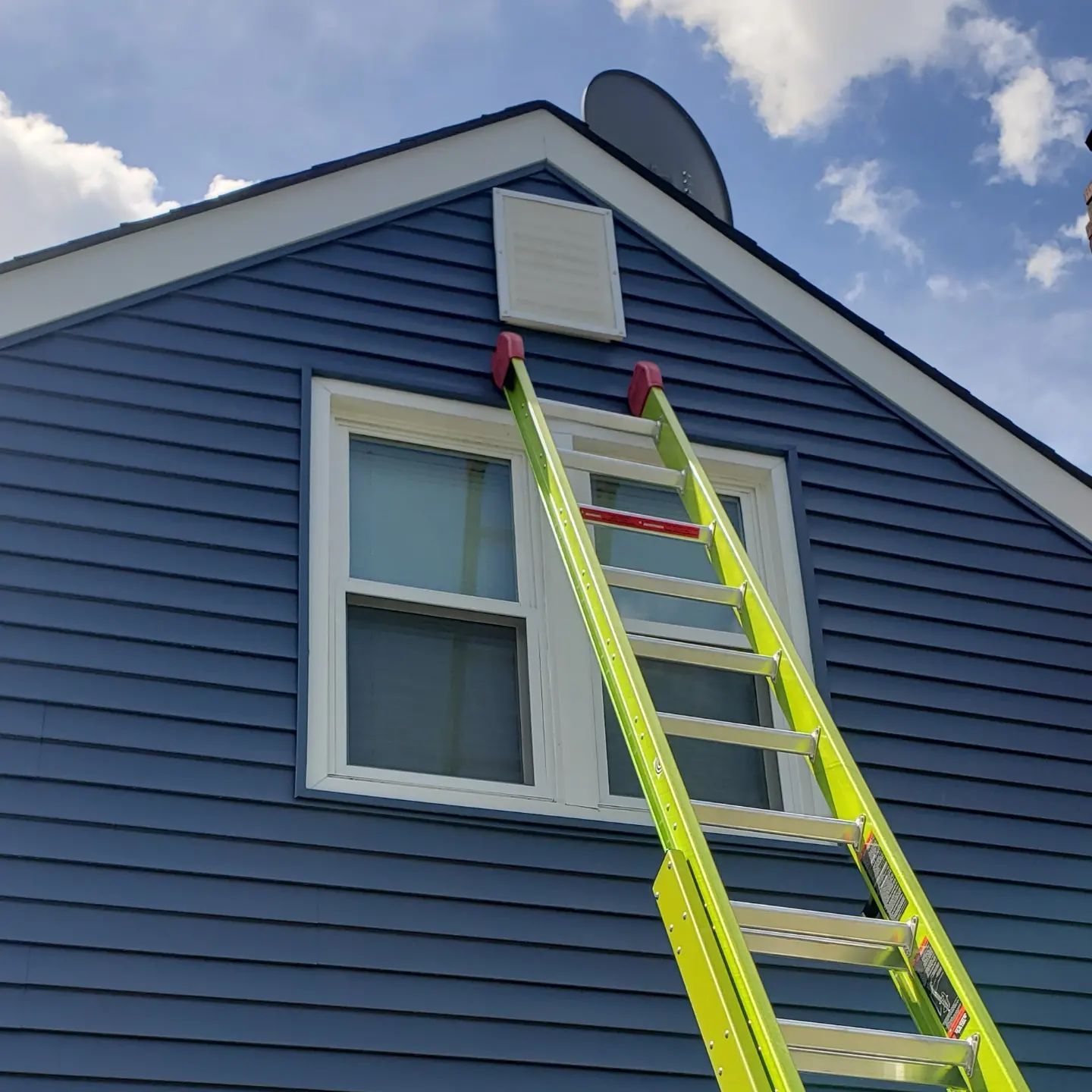 A ladder is sitting on the side of a blue house