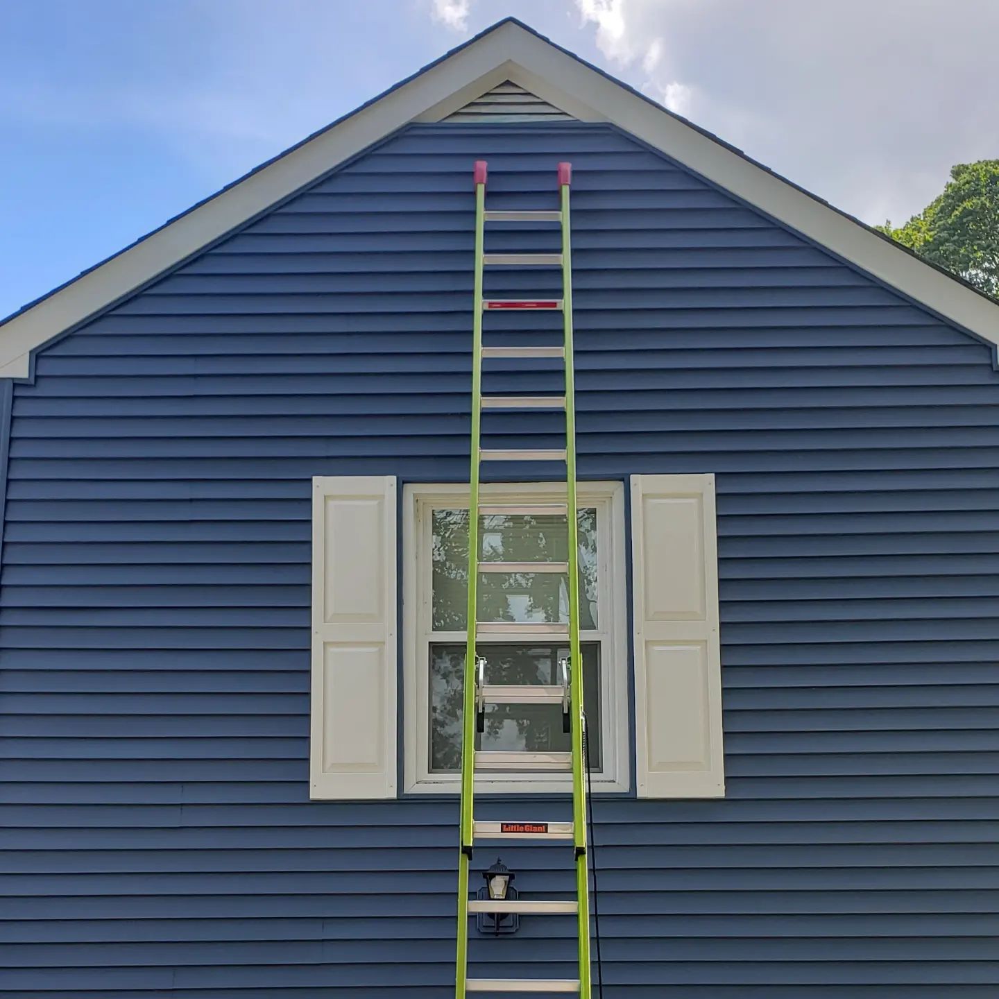 A green ladder is sitting on the side of a blue house.