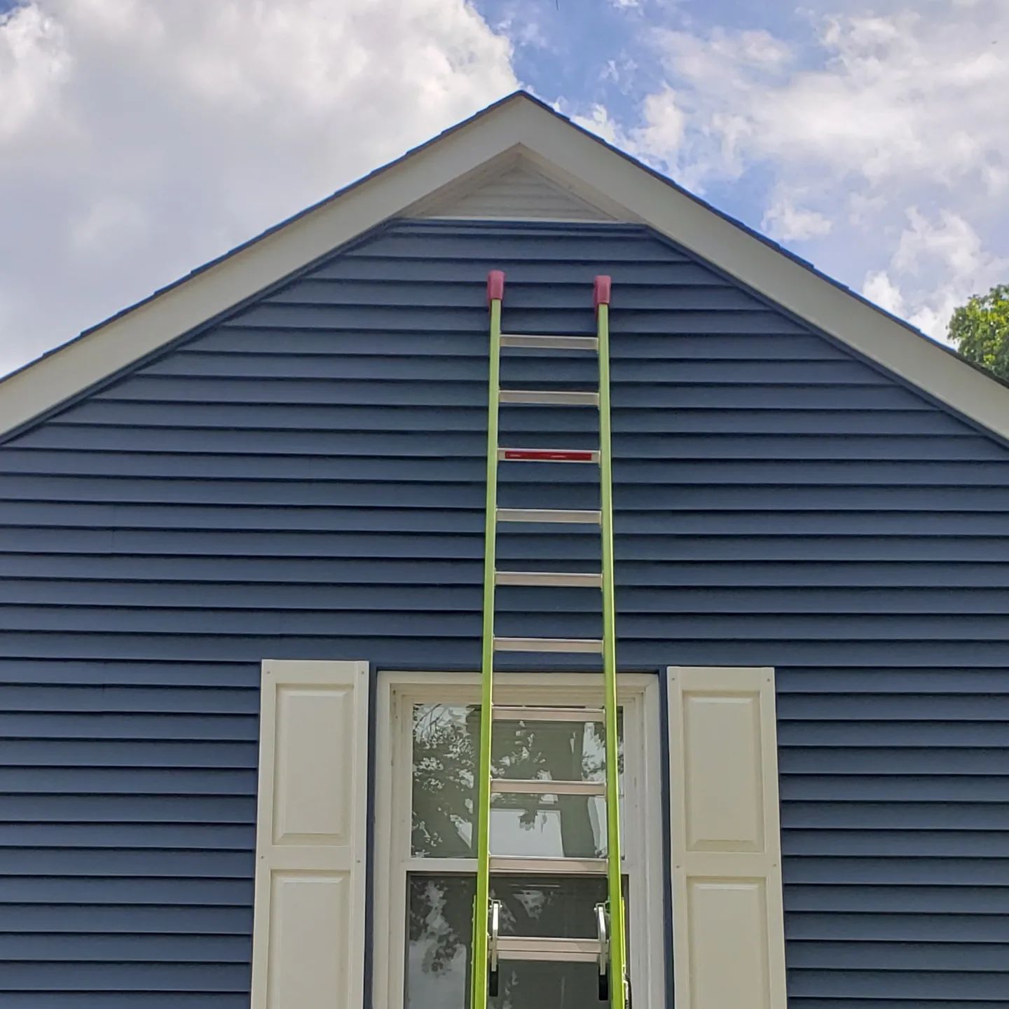 A ladder is leaning against the side of a blue house.