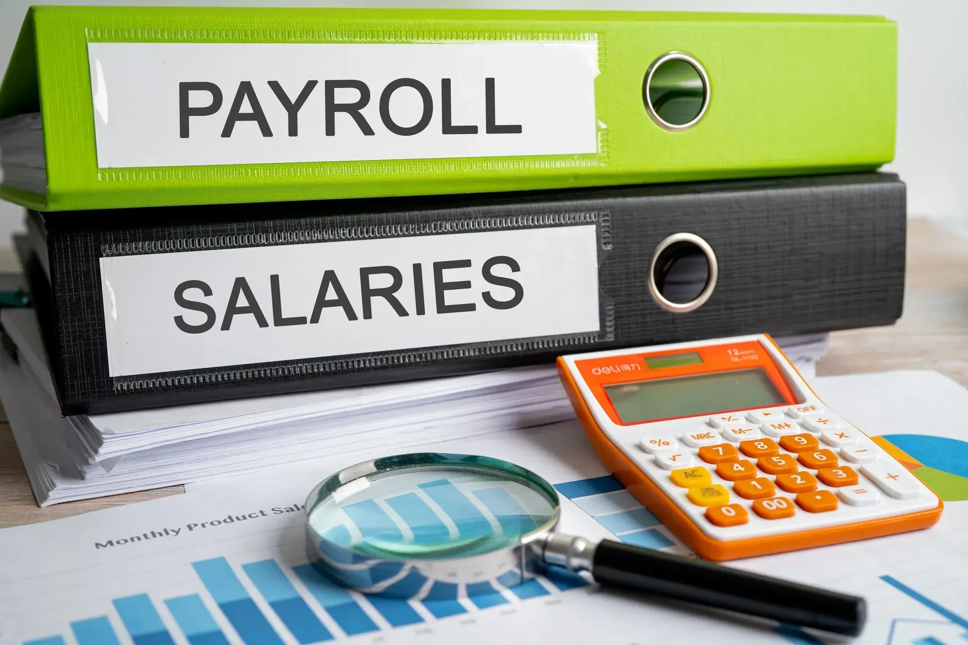 A calculator , magnifying glass , and pen are on a table next to a stack of payroll binders.