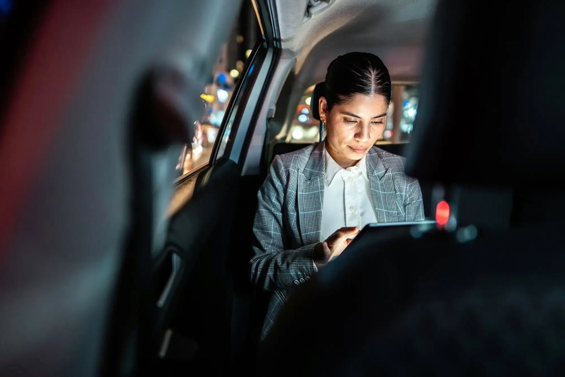 Two business professionals in suits shake hands by a white taxi cab in an urban setting.