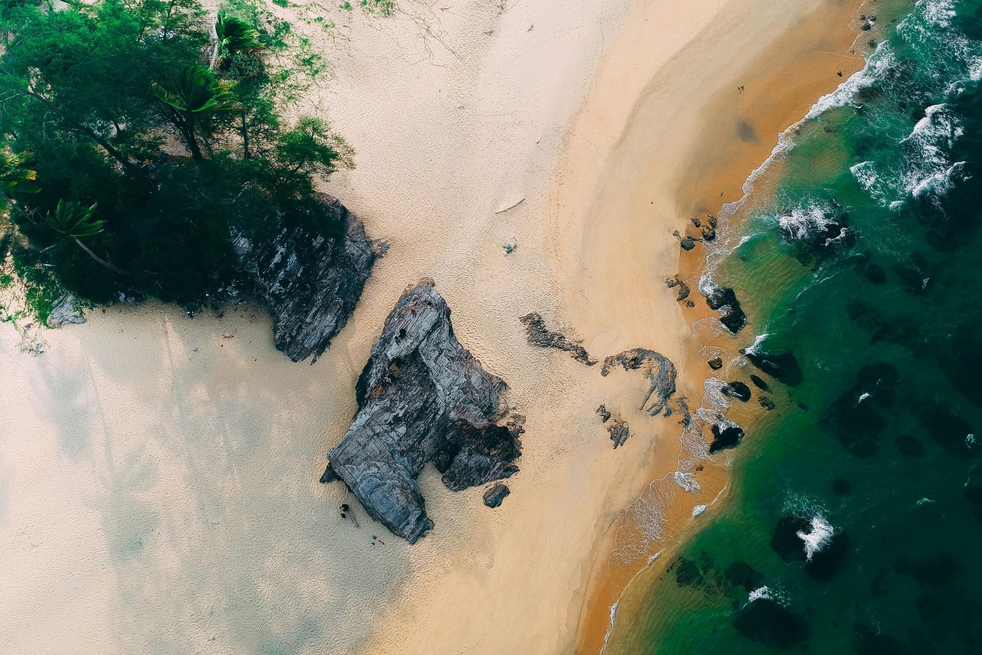 Waves crashing onto a rocky, brown shoreline; sandy beach visible.