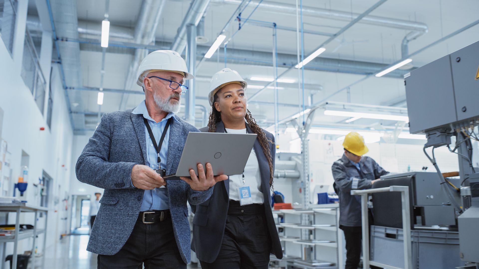 A man in a suit and glasses is standing in a factory with his hands in his pockets.