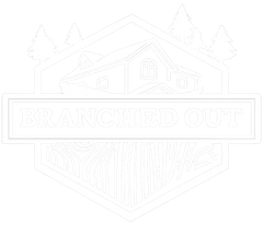A white logo on a black background featuring a house outline, pine trees, and a wood-grain pattern inside a hexagon.