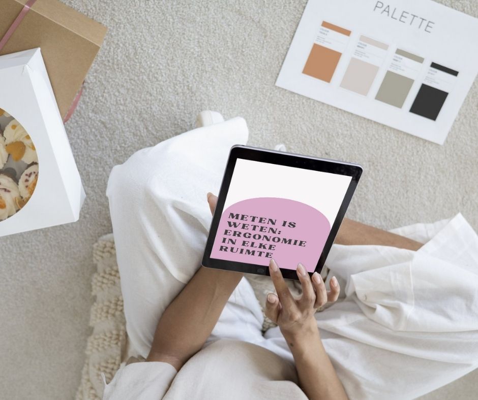 Persoon houdt tablet met tekst vast; rustend op kleed; kleurenpalet en dessertdoos in de buurt.