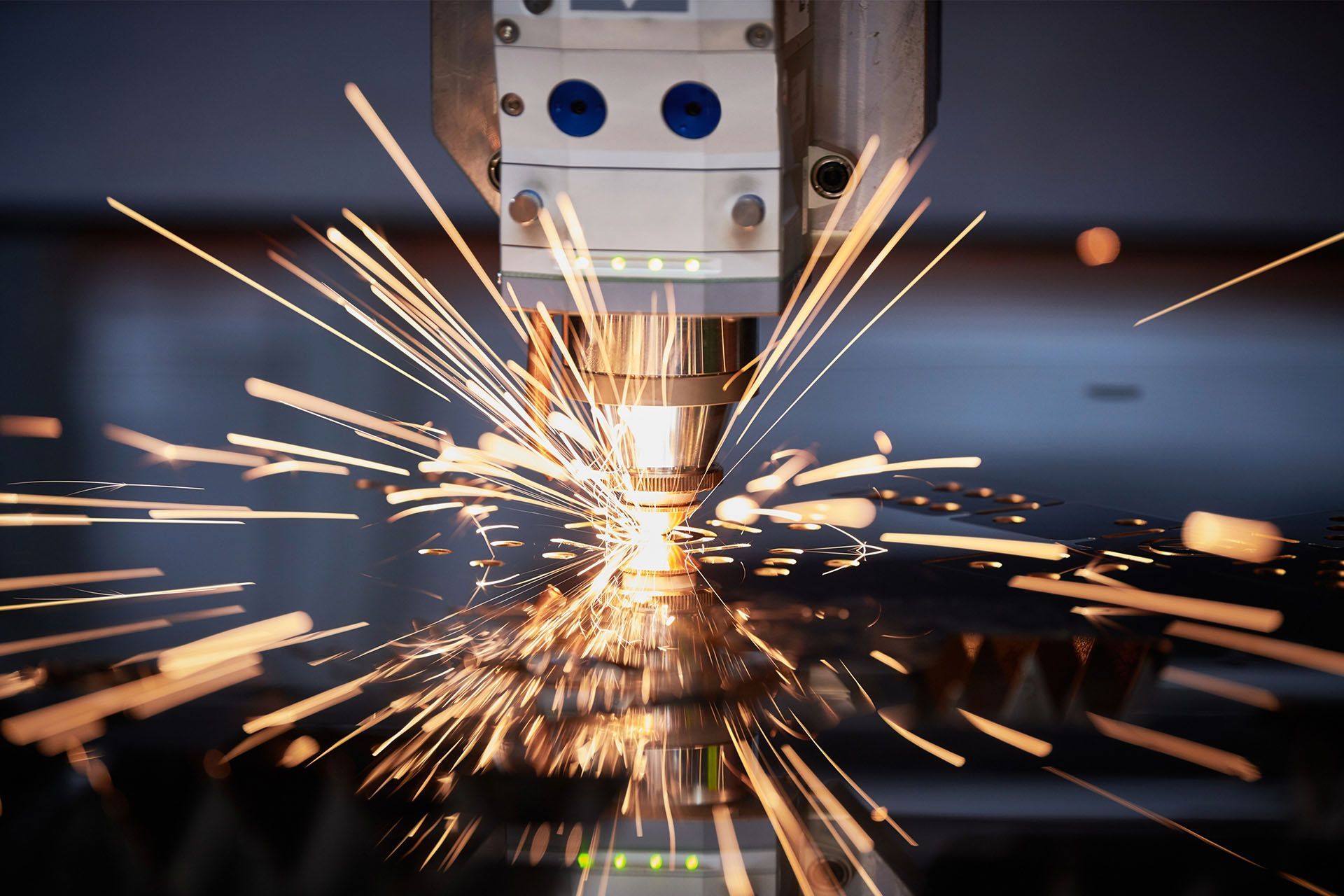 Laser cutter in action, sparks flying as it cuts through metal sheet.