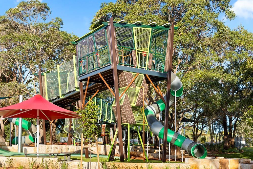A tree house with a slide and umbrellas in a park.