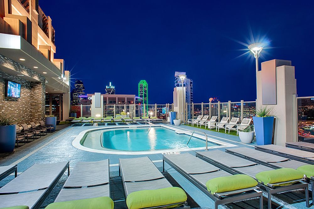 A large swimming pool is surrounded by lounge chairs at night.