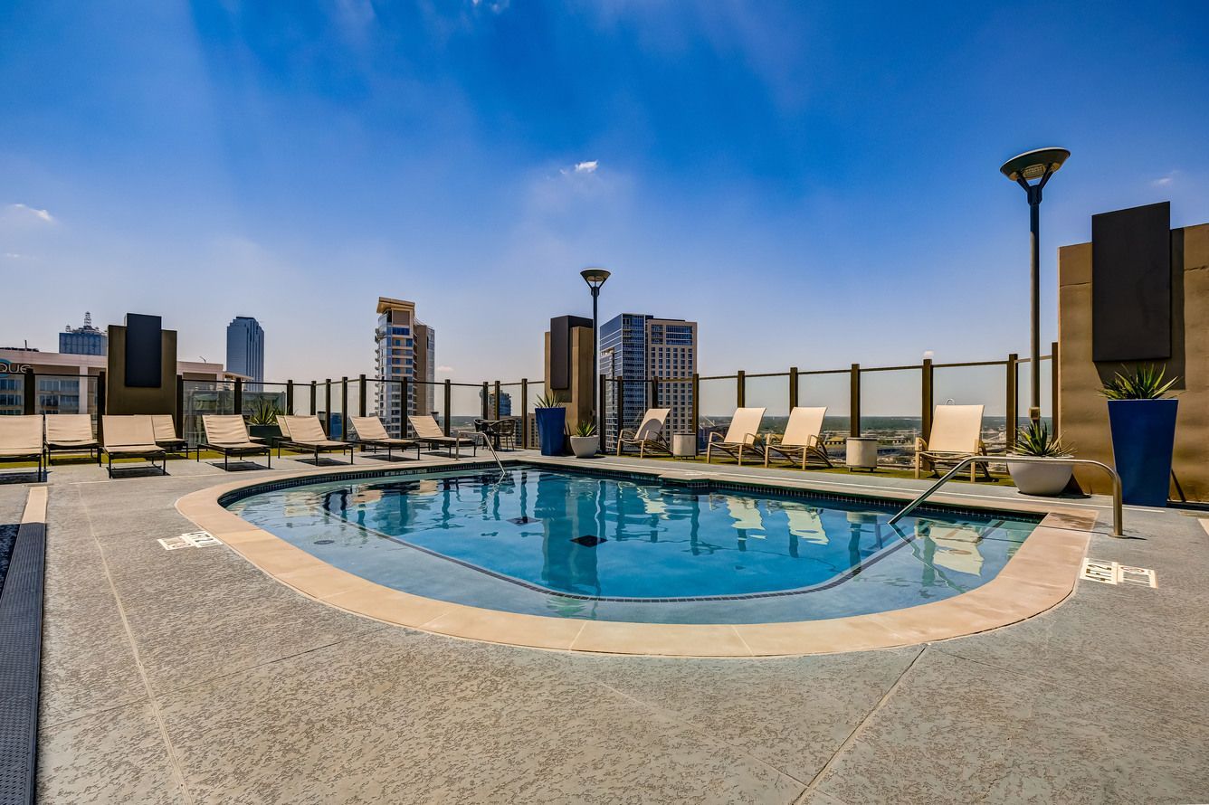 A large swimming pool with chairs around it and a city in the background.