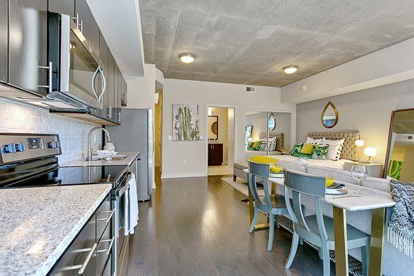 A kitchen with stainless steel appliances , a table , chairs and a bed.