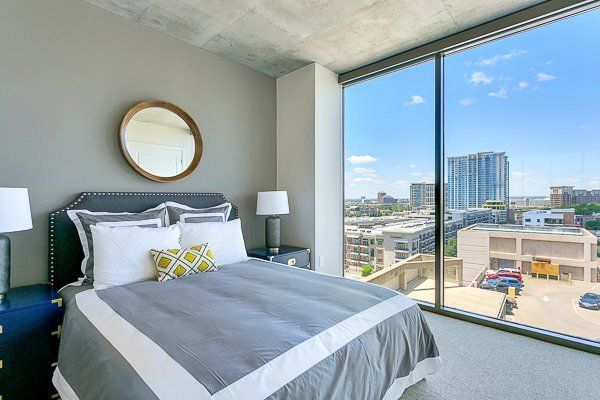 A bedroom with a large bed and a large window with a view of the city.