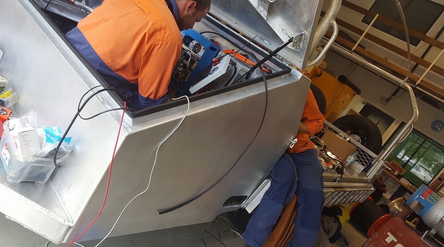 A Man In An Orange Shirt Is Working On A Machine In A Garage — PASMA Electrical In Portsmith, QLD