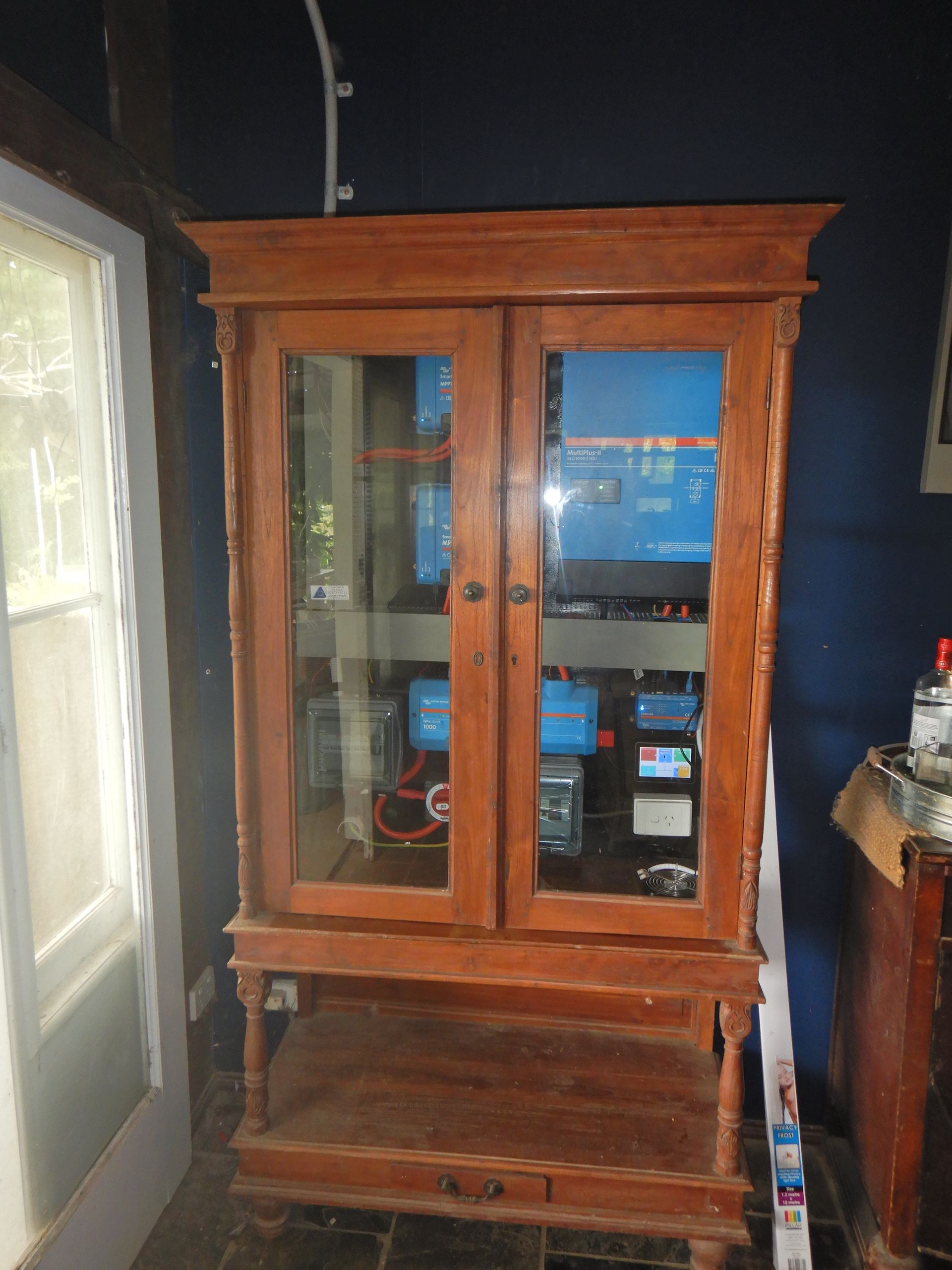 A Wooden Cabinet With Glass Doors Is Sitting In A Room Next To A Window — PASMA Electrical In Portsmith, QLD