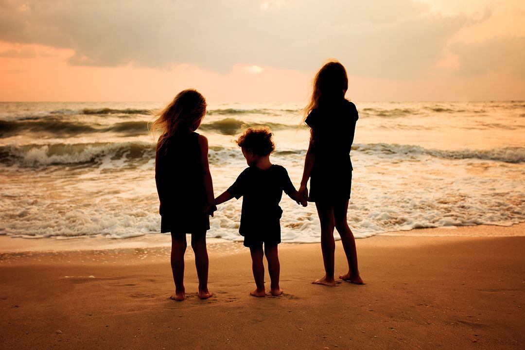three children holding hands on a beach