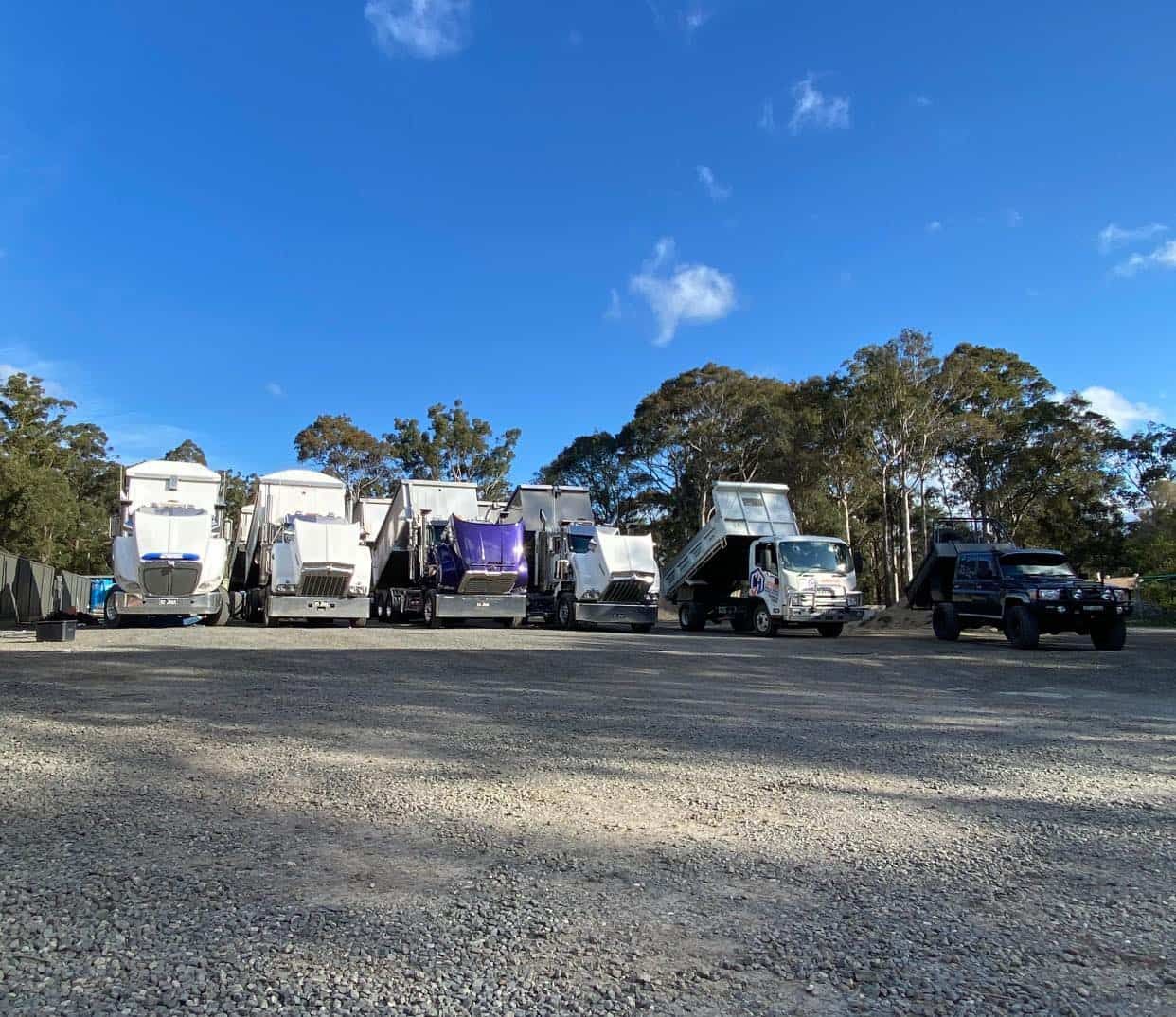 A Row Of Garbage Trucks Are Parked In A Gravel Lot — JMAK Haulage & Landscapes Supplies In Falls Creek, NSW