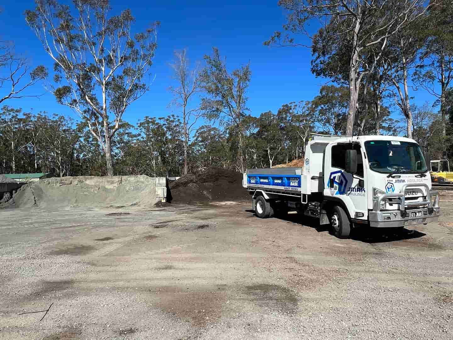A Dump Truck Is Parked In A Dirt Lot With Trees In The Background — JMAK Haulage & Landscapes Supplies In Falls Creek, NSW