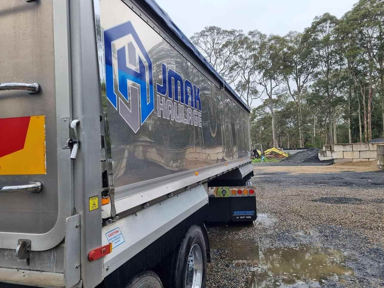 A Dump Truck Is Parked In A Dirt Lot With Trees In The Background — JMAK Haulage & Landscapes Supplies In Berry, NSW
