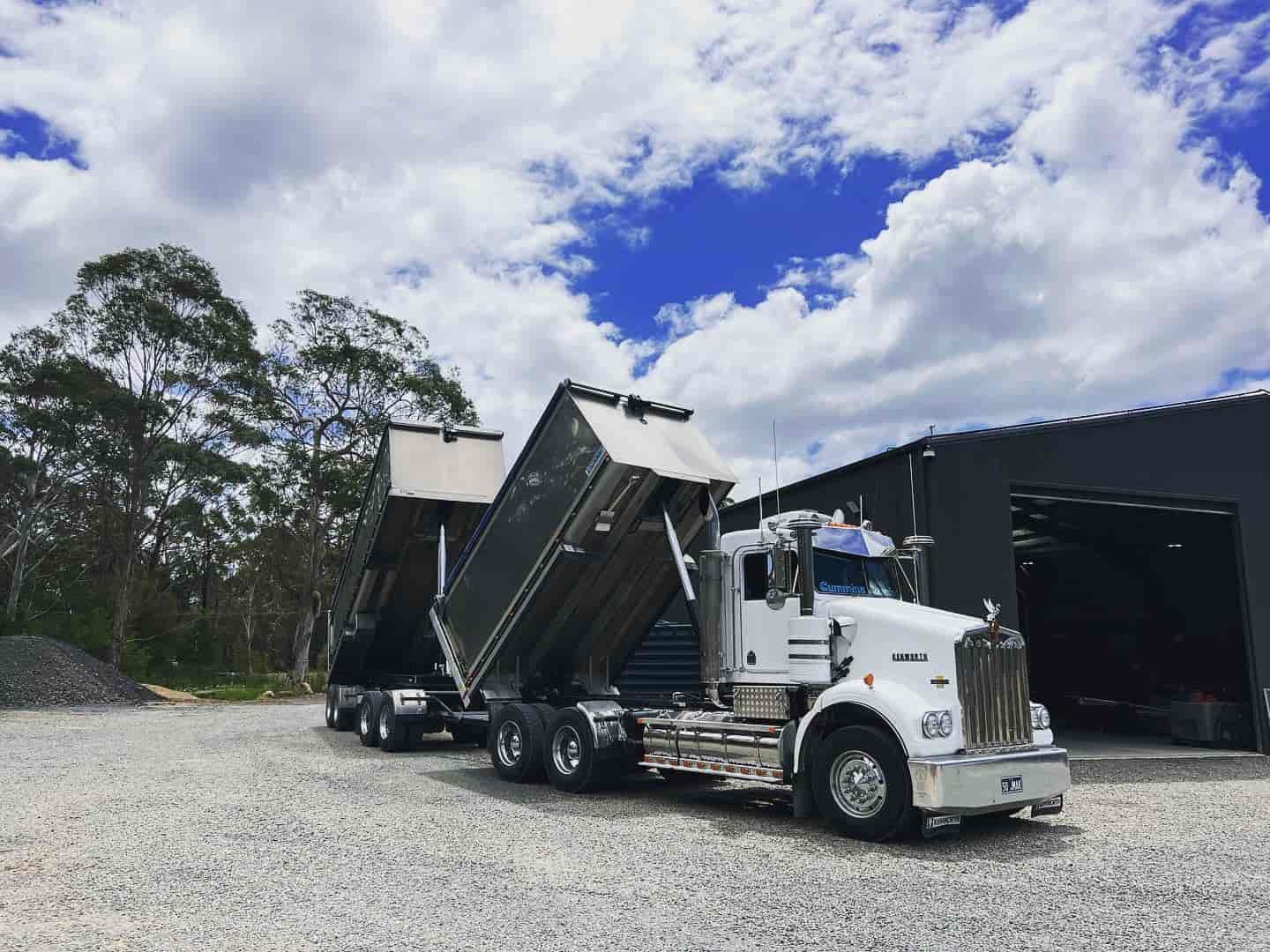 A Dump Truck Is Parked In A Gravel Lot In Front Of A Building — JMAK Haulage & Landscapes Supplies In Nowra, NSW