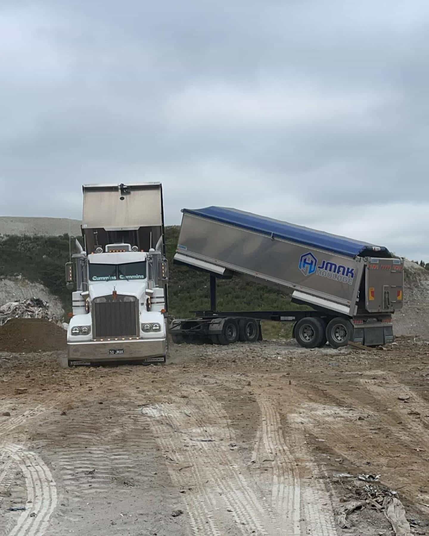 A Dump Truck Is Driving Down A Dirt Road Next To A Bulldozer — JMAK Haulage & Landscapes Supplies In Falls Creek, NSW
